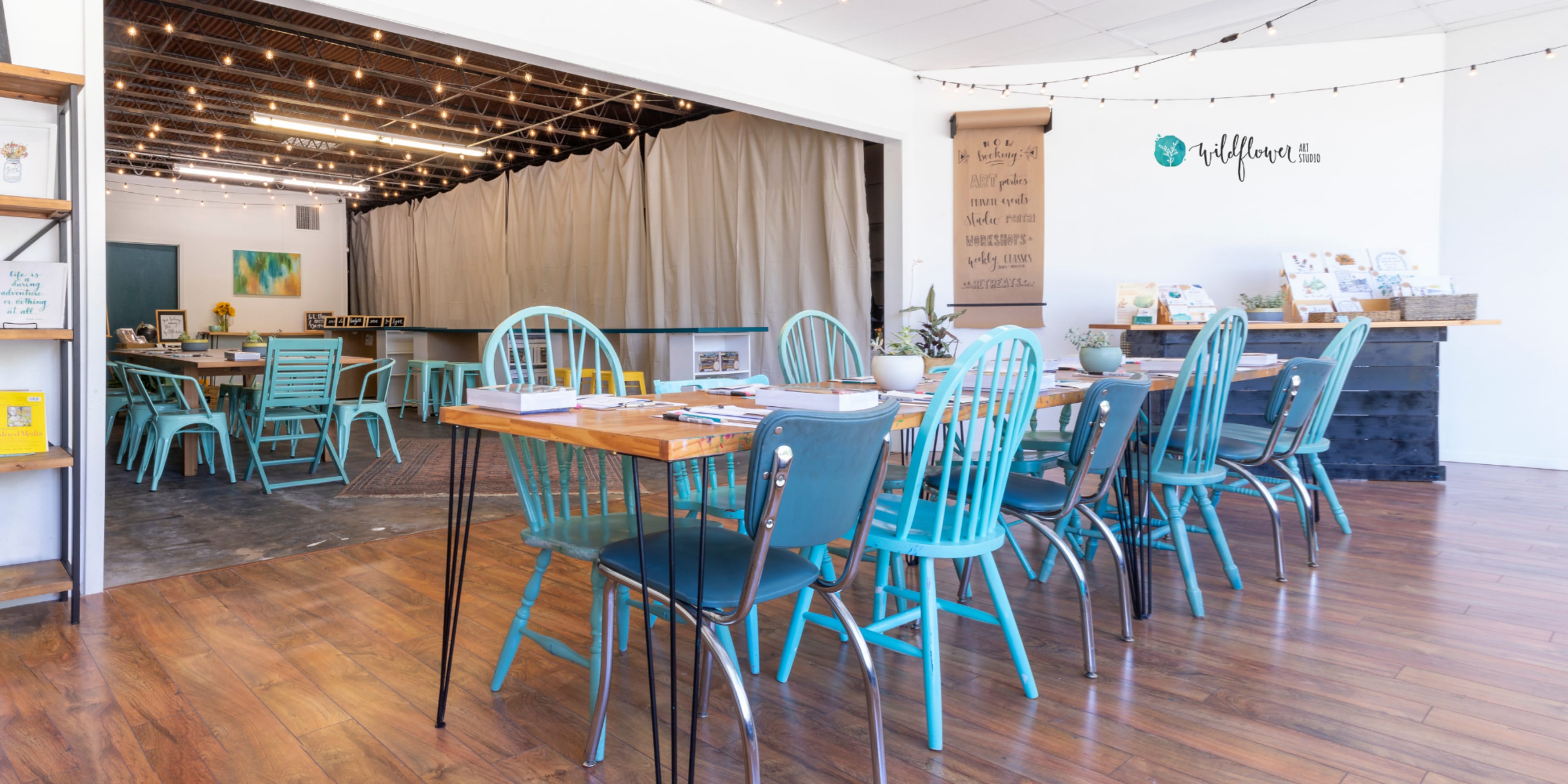 A spacious interior features wooden tables surrounded by teal chairs, with a partitioned area in the background.