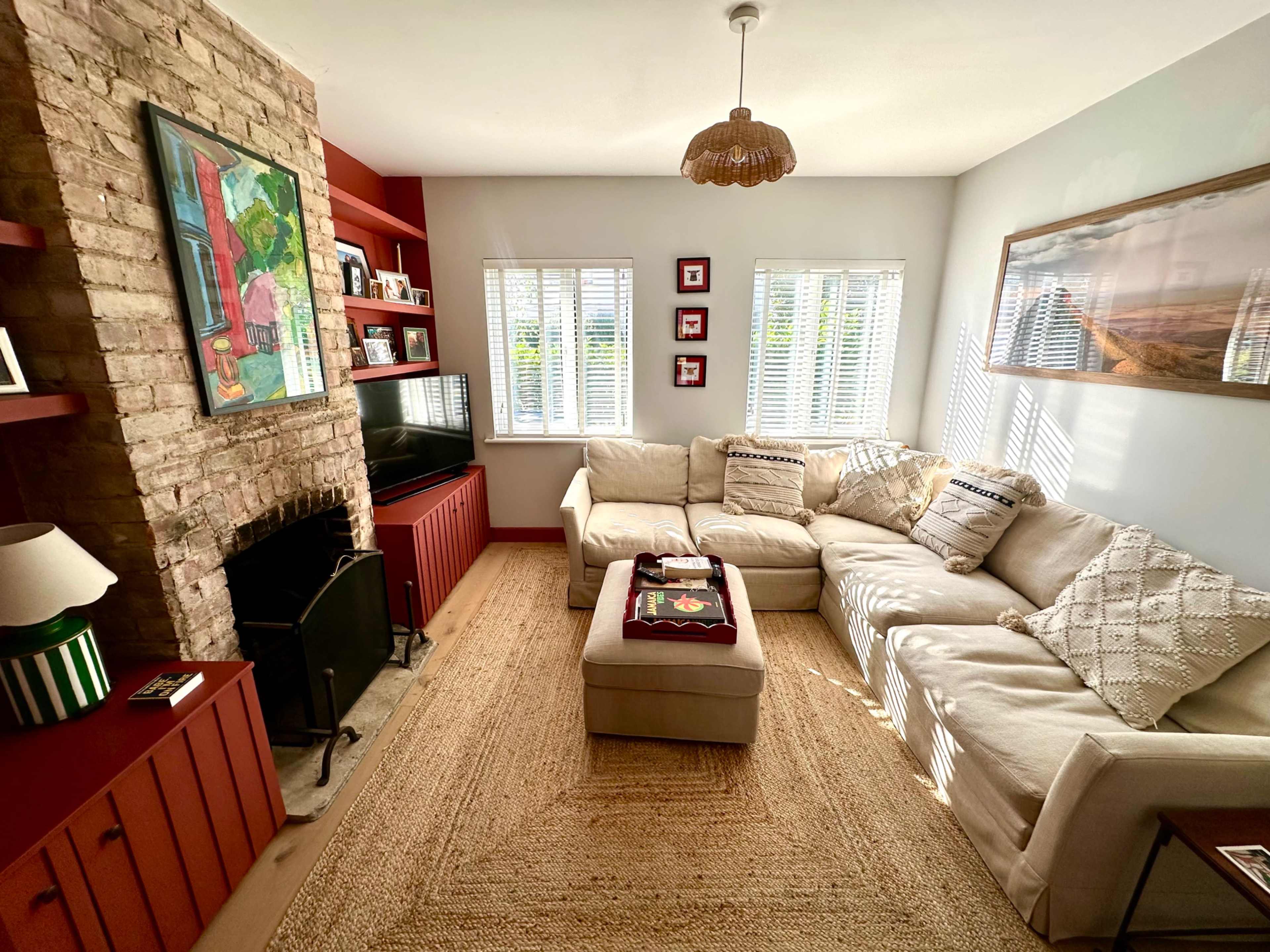 The image shows a cozy living room featuring a sectional sofa, a stone fireplace, and bright, natural light coming through the windows.