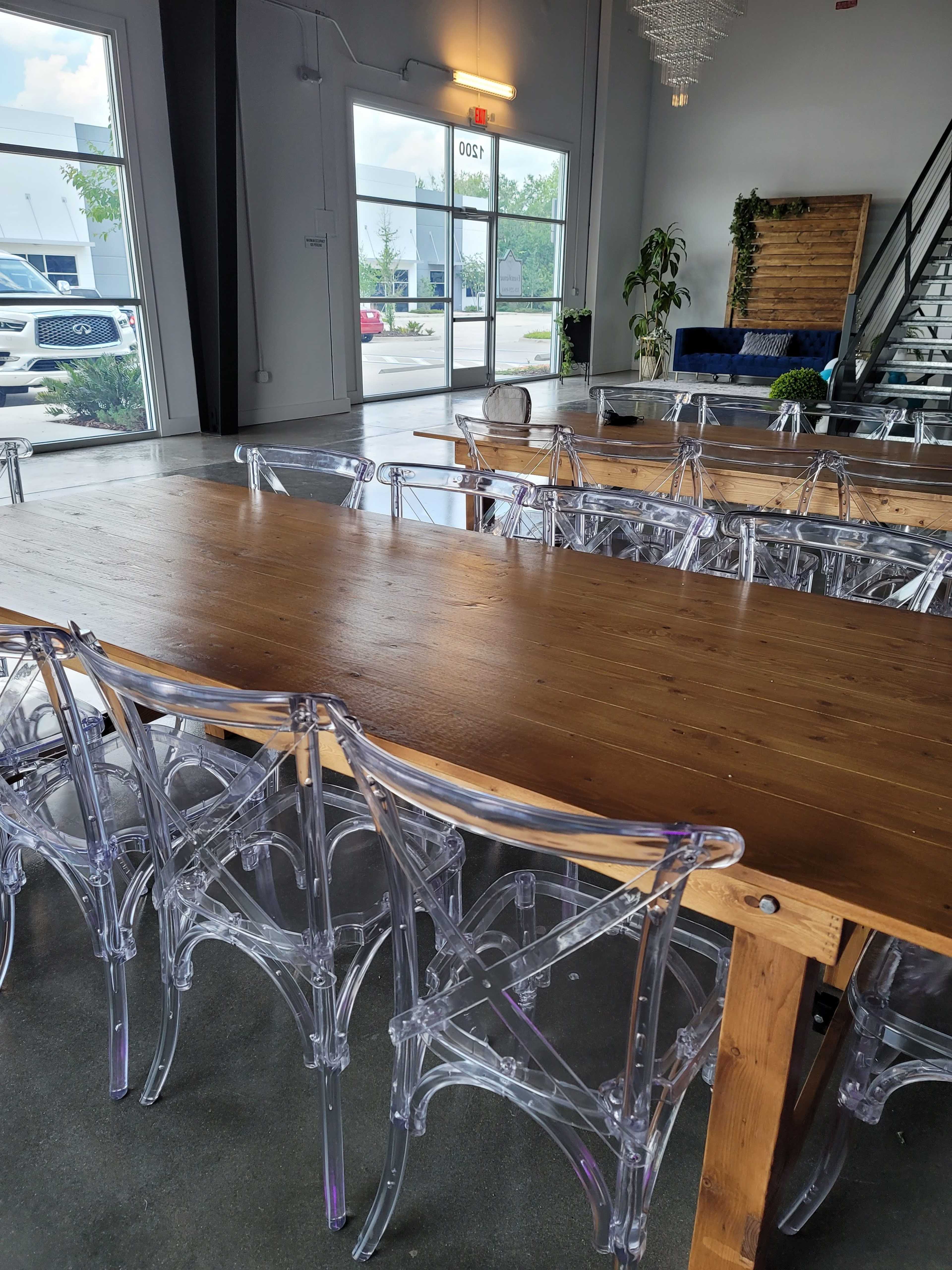 A long wooden table surrounded by transparent acrylic chairs is set up in a bright, modern room with large windows.