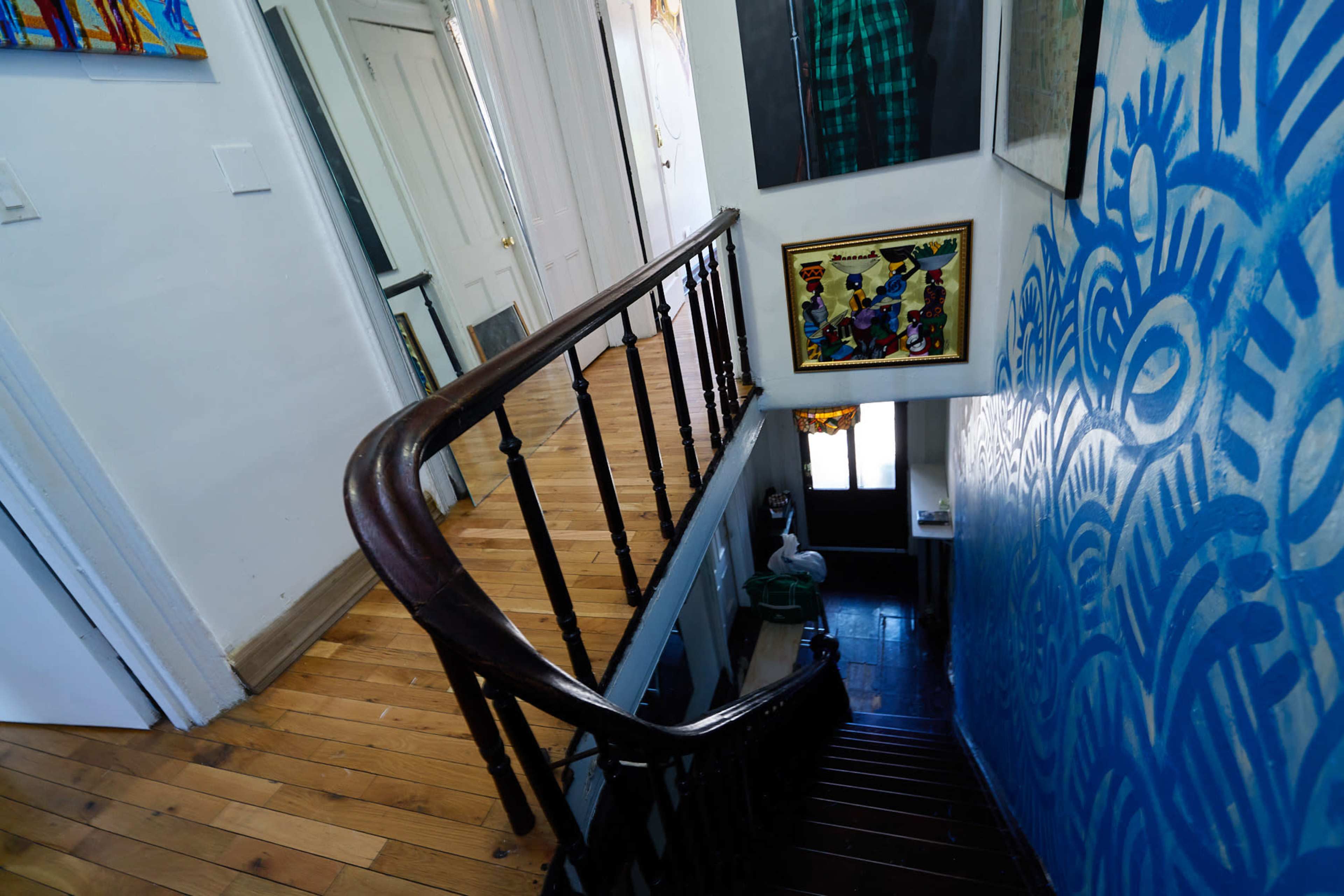 A wooden staircase with a curved railing leads down to a hallway decorated with artwork and a blue patterned wall.