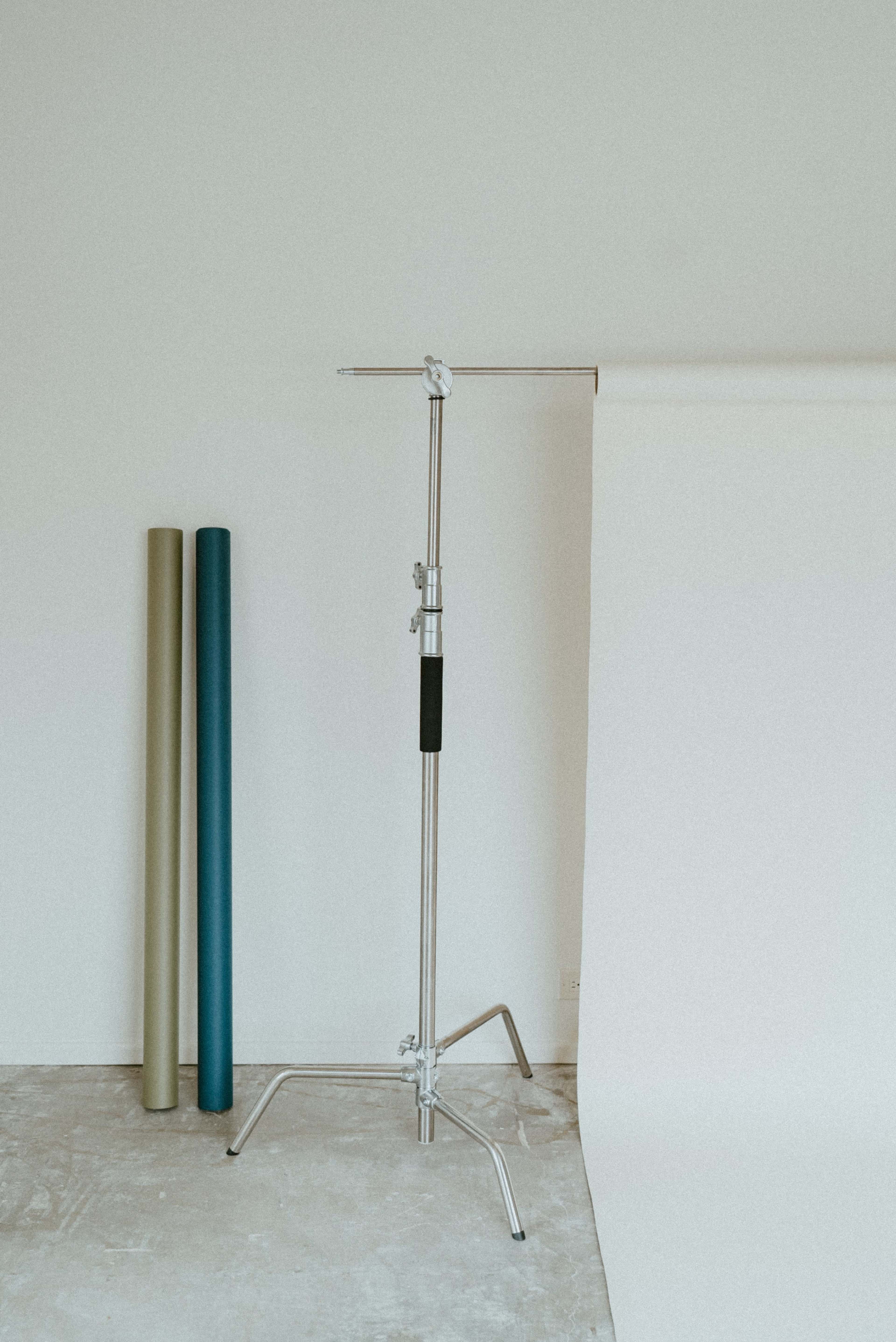 A silver backdrop stand is positioned beside three rolls of colored paper against a light background.