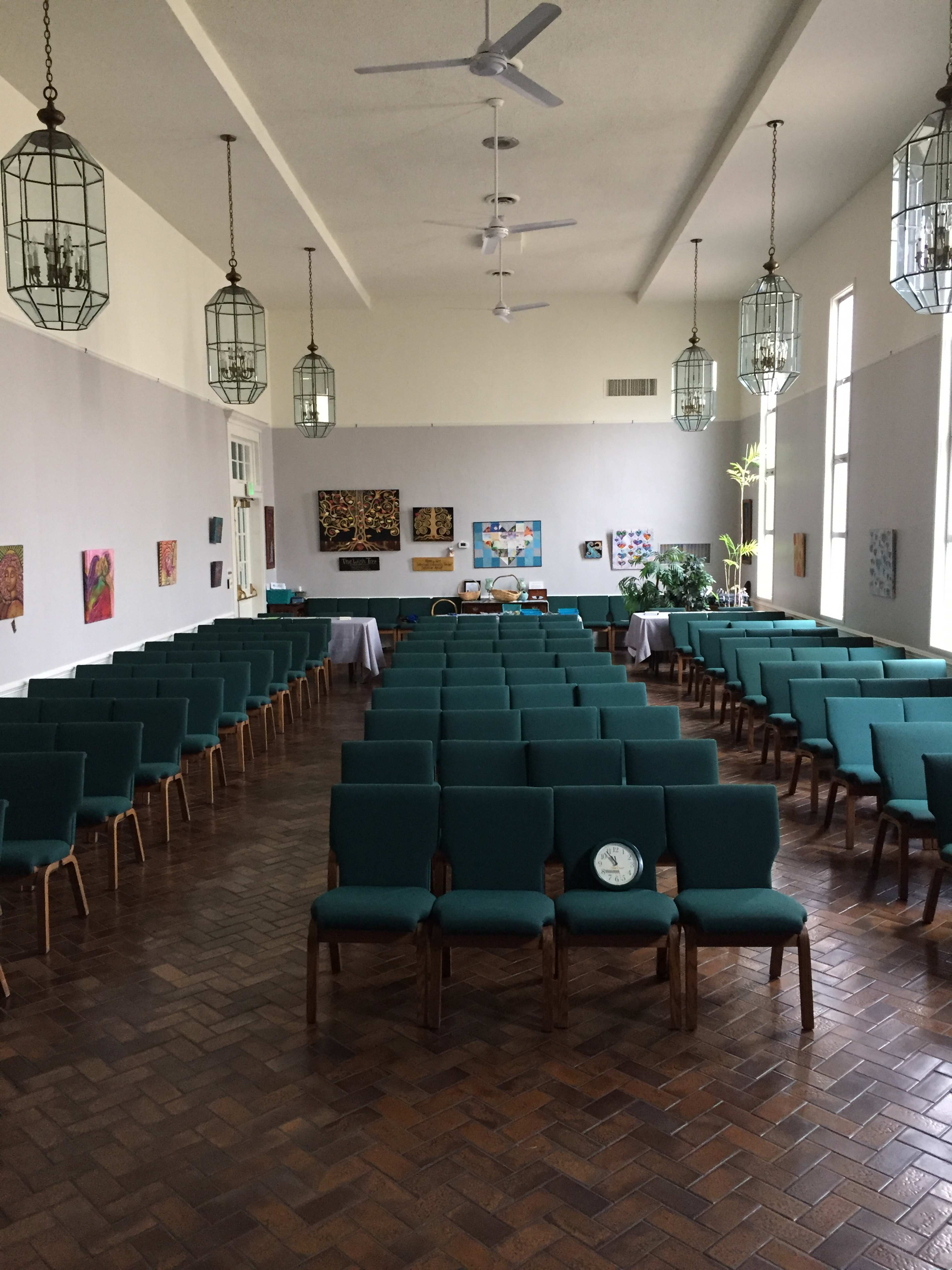 A spacious community hall with rows of green chairs arranged in a grid, adorned with hanging lanterns and colorful artwork on the walls.