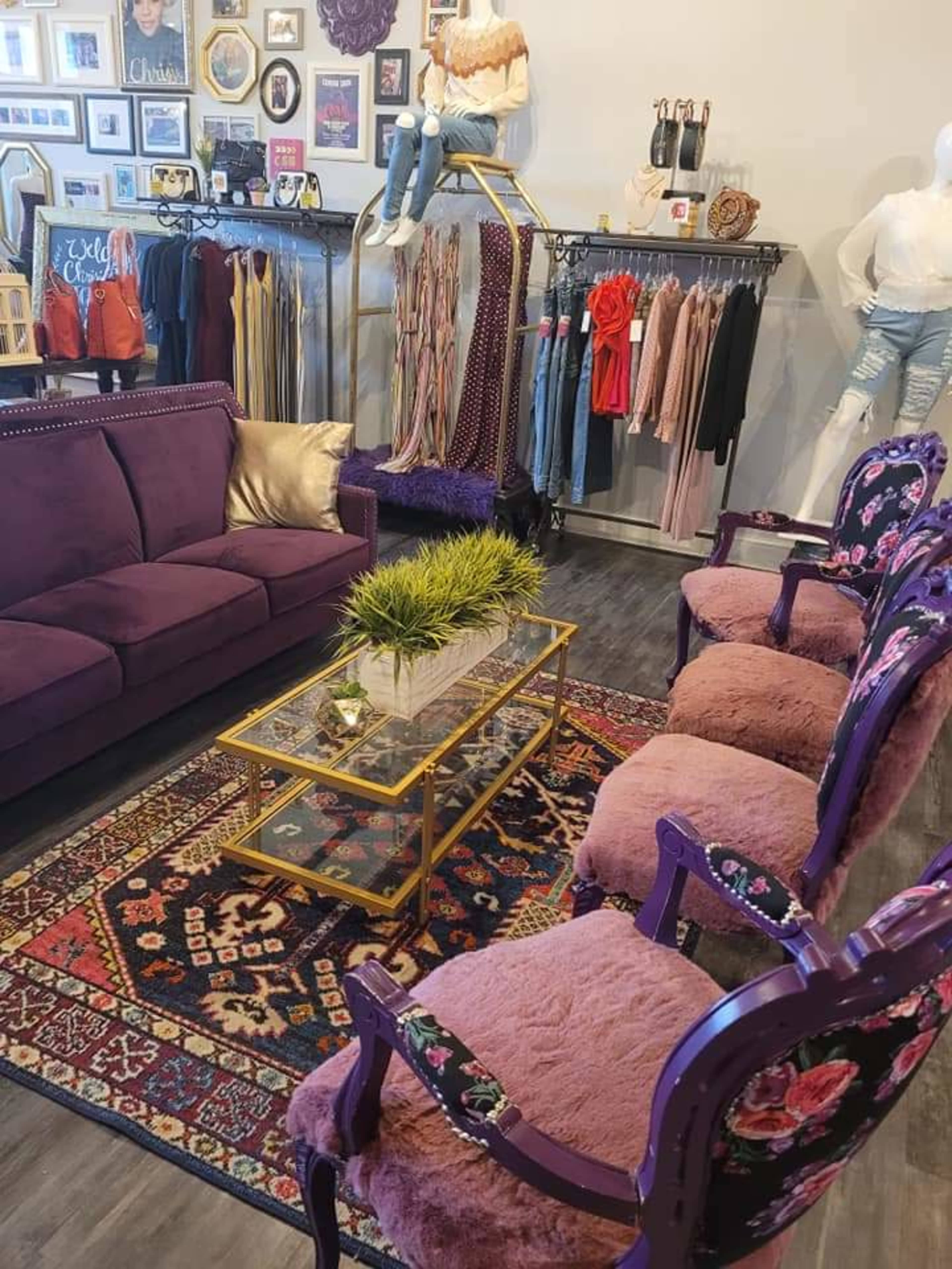 A boutique interior featuring a purple sofa, four purple upholstered chairs, a glass coffee table, and clothing displays along the walls.