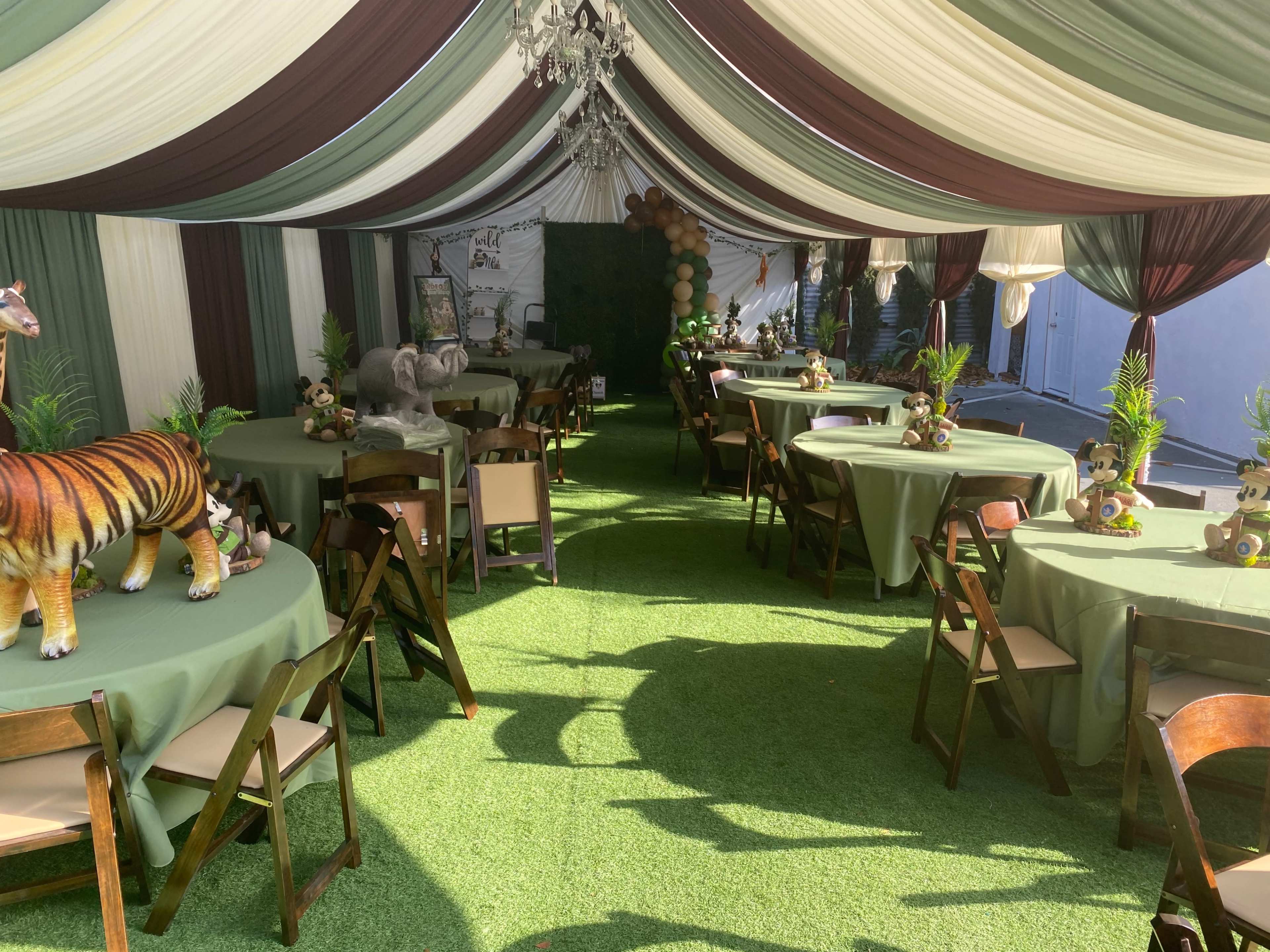 A decorated party tent with green and brown draped fabrics, tables covered in green tablecloths, and themed animal centerpieces.