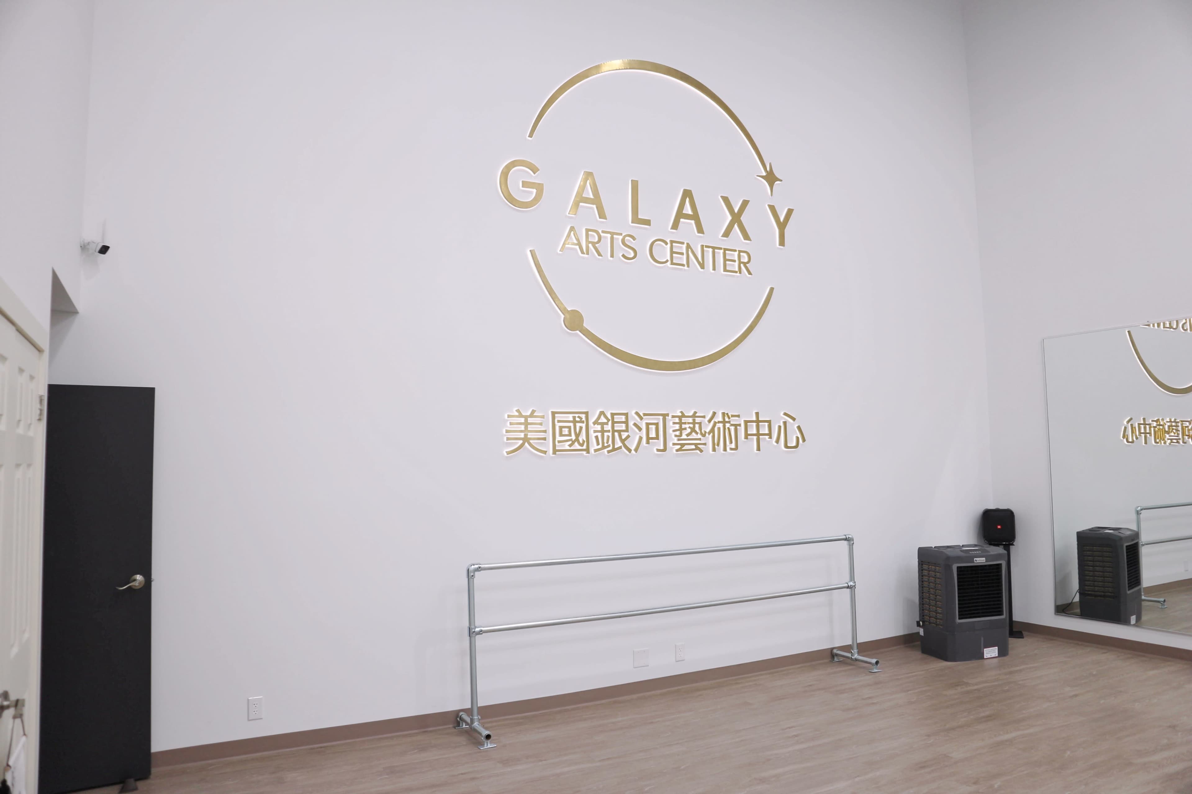 A minimalist interior of an arts center featuring a gold wall sign that reads "GALAXY ARTS CENTER" in English and Chinese.