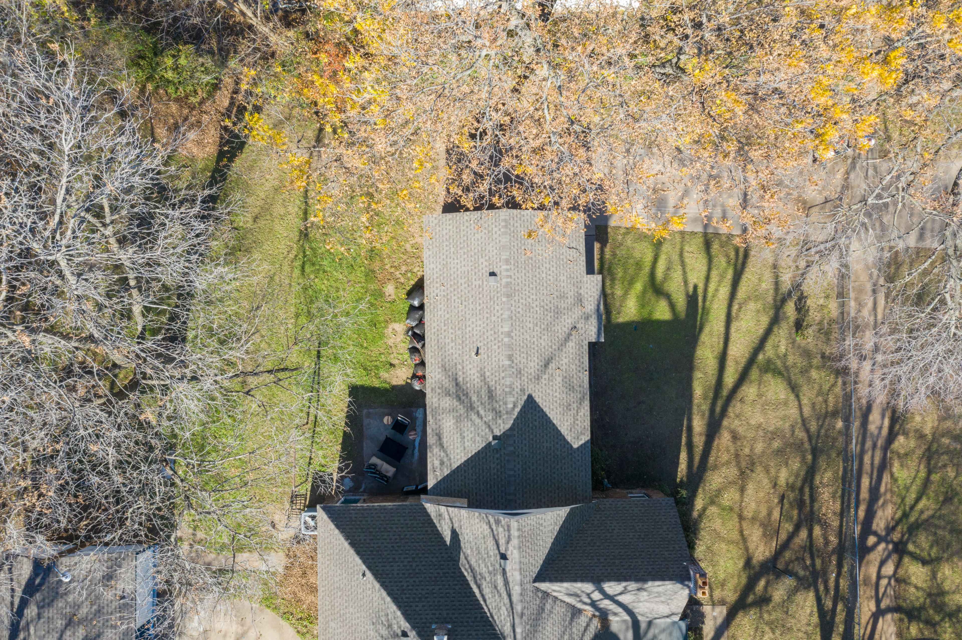 The image shows an aerial view of residential houses and surrounding area, with a large tree casting shadows on the lawns.