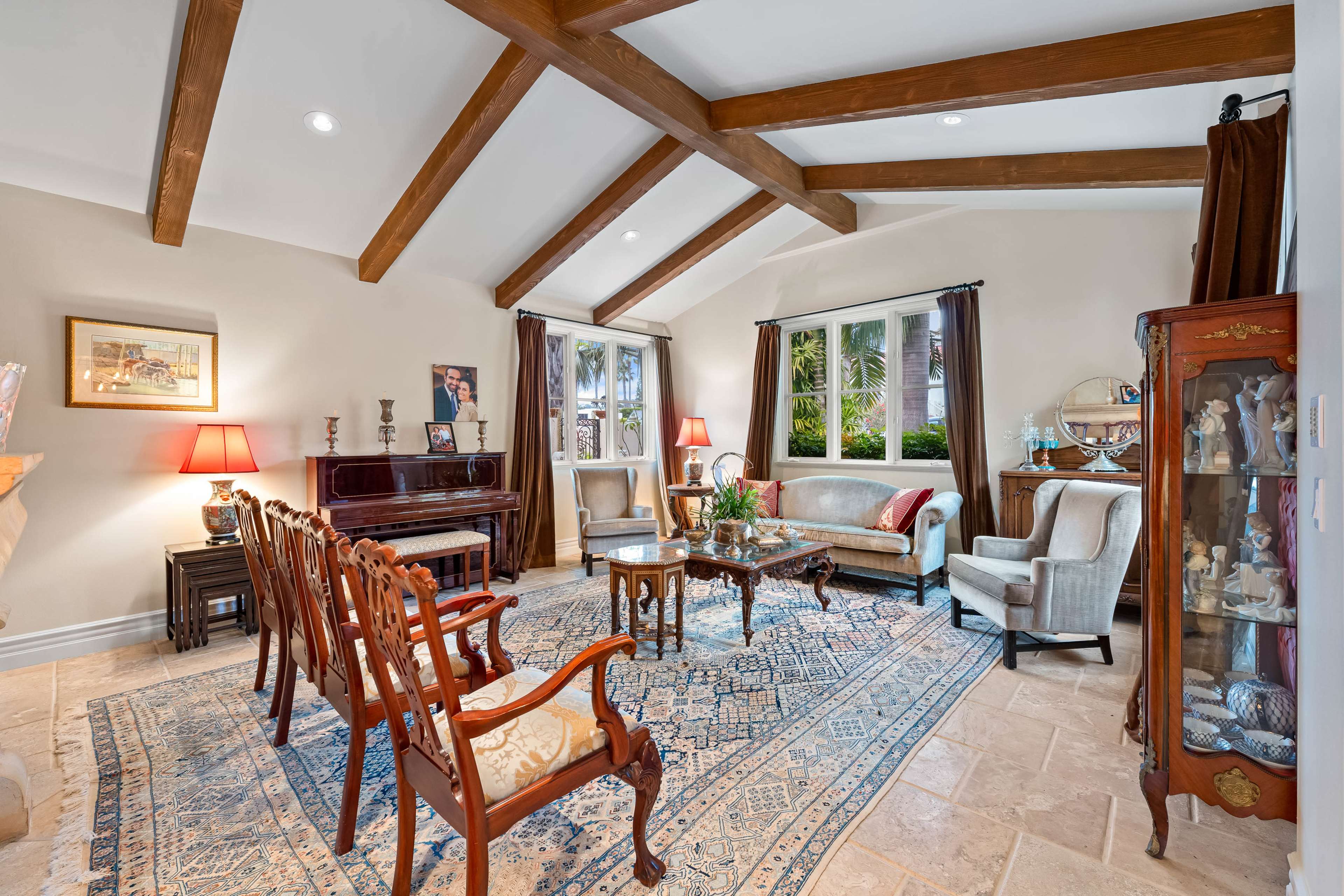 The living room features a grand piano, a set of wooden chairs, a coffee table with a floral arrangement, and large windows allowing natural light.