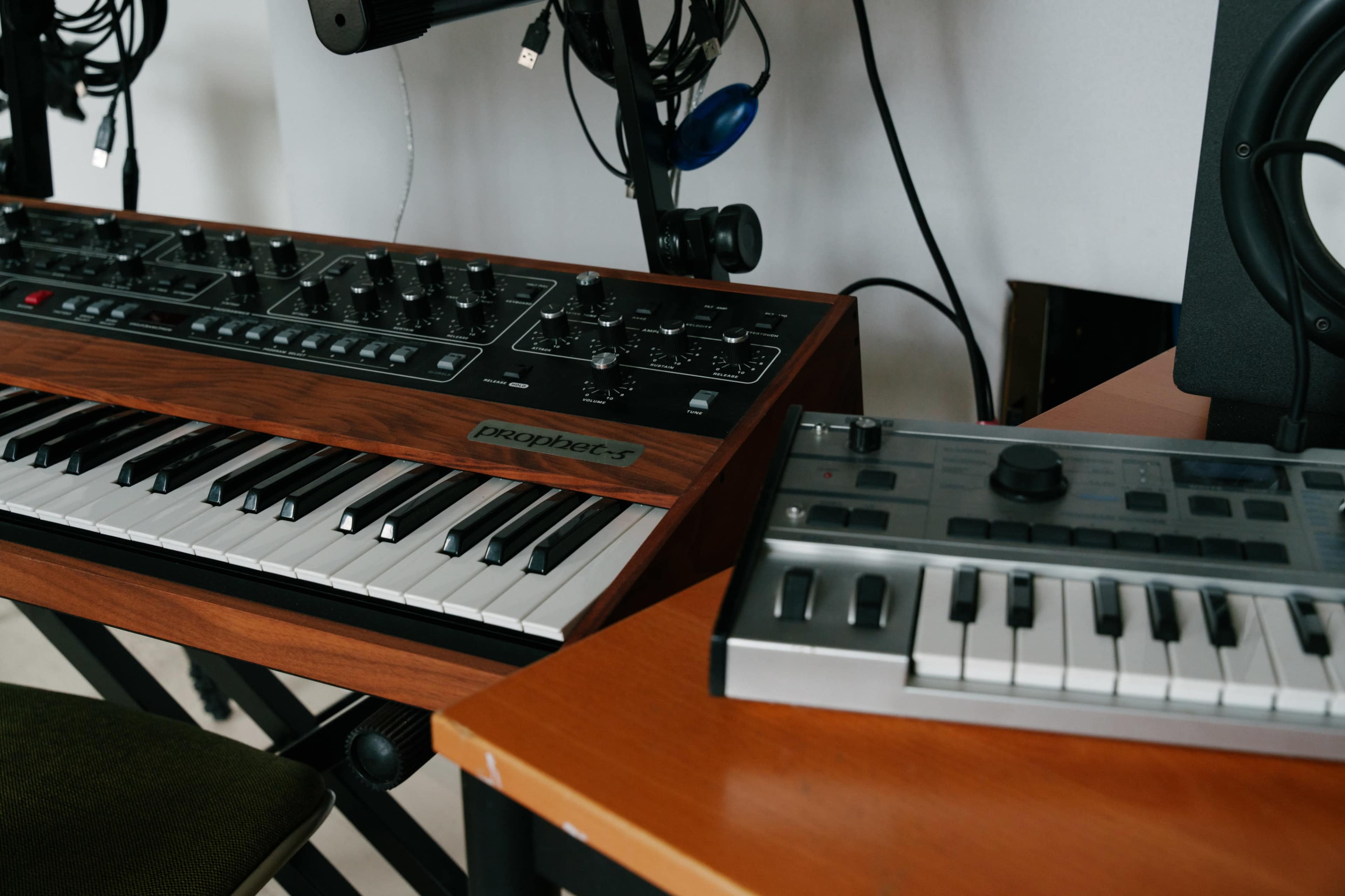 A wooden synthesizer with a keyboard and various knobs next to a smaller, silver music controller on a table.