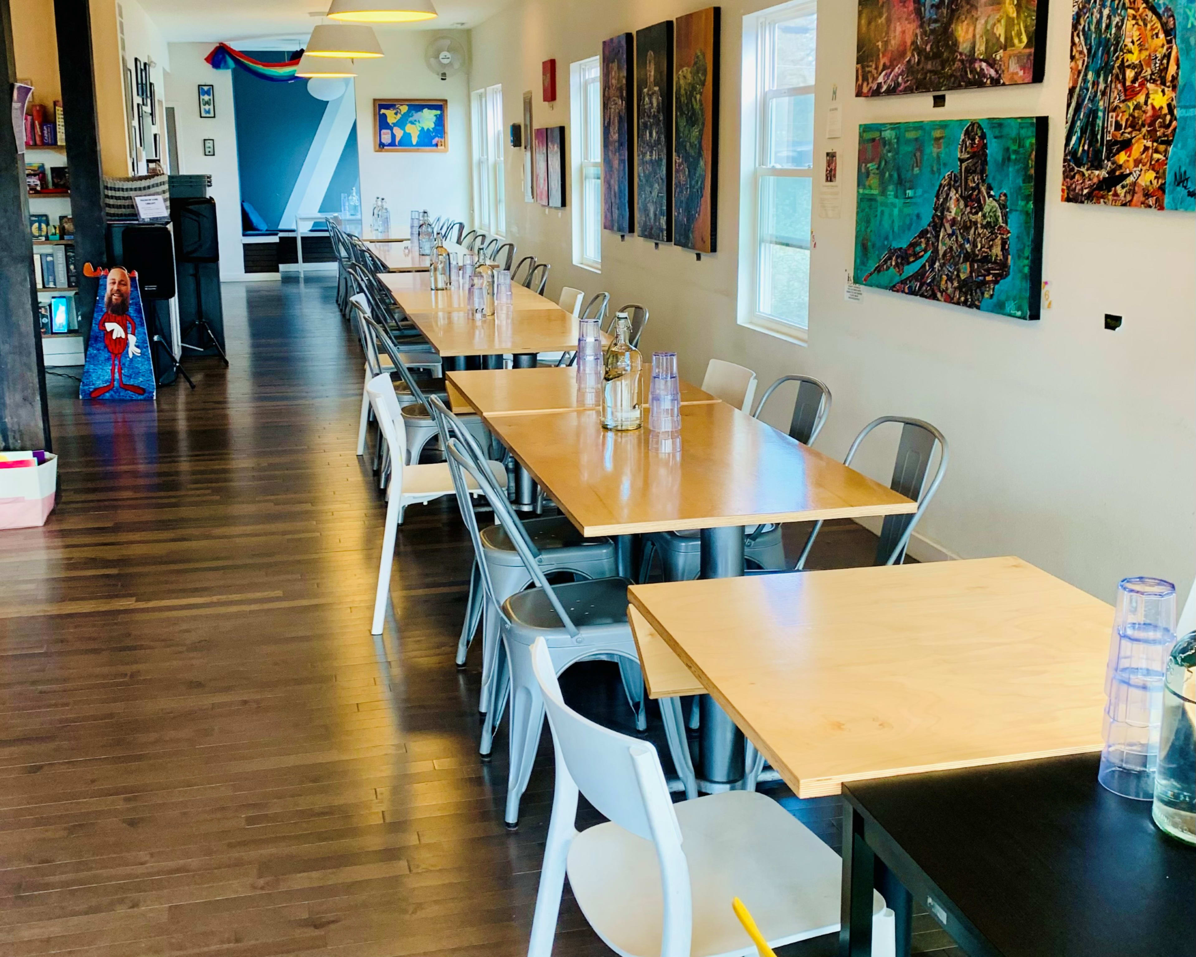 A long row of tables with chairs in a well-lit room adorned with colorful artwork on the walls.