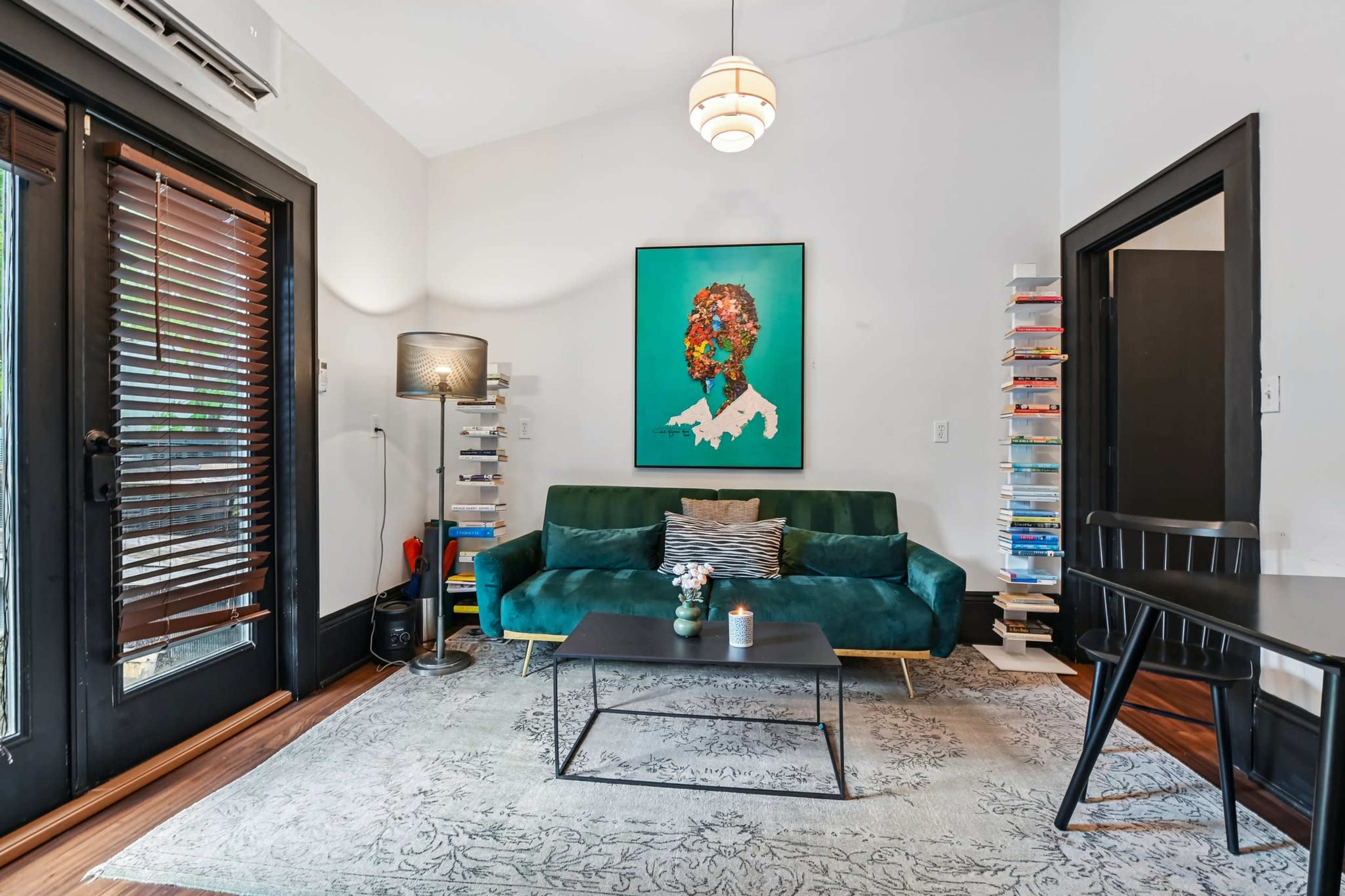 The image shows a modern living room with a teal sofa, a black coffee table, a colorful artwork on the wall, and a small dining table.