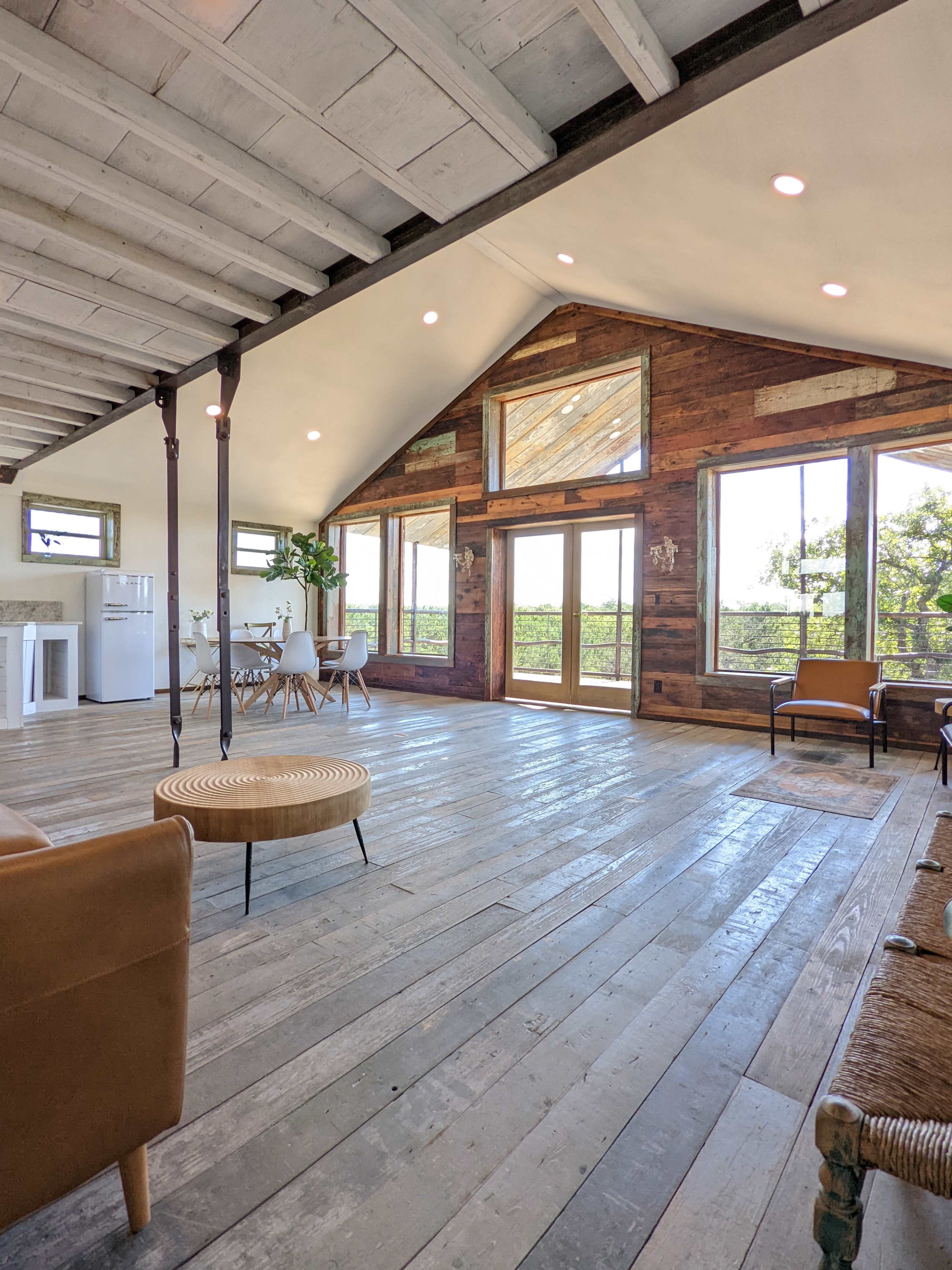 A spacious interior with wooden floors, large windows, and rustic decor, featuring a seating area and dining space.