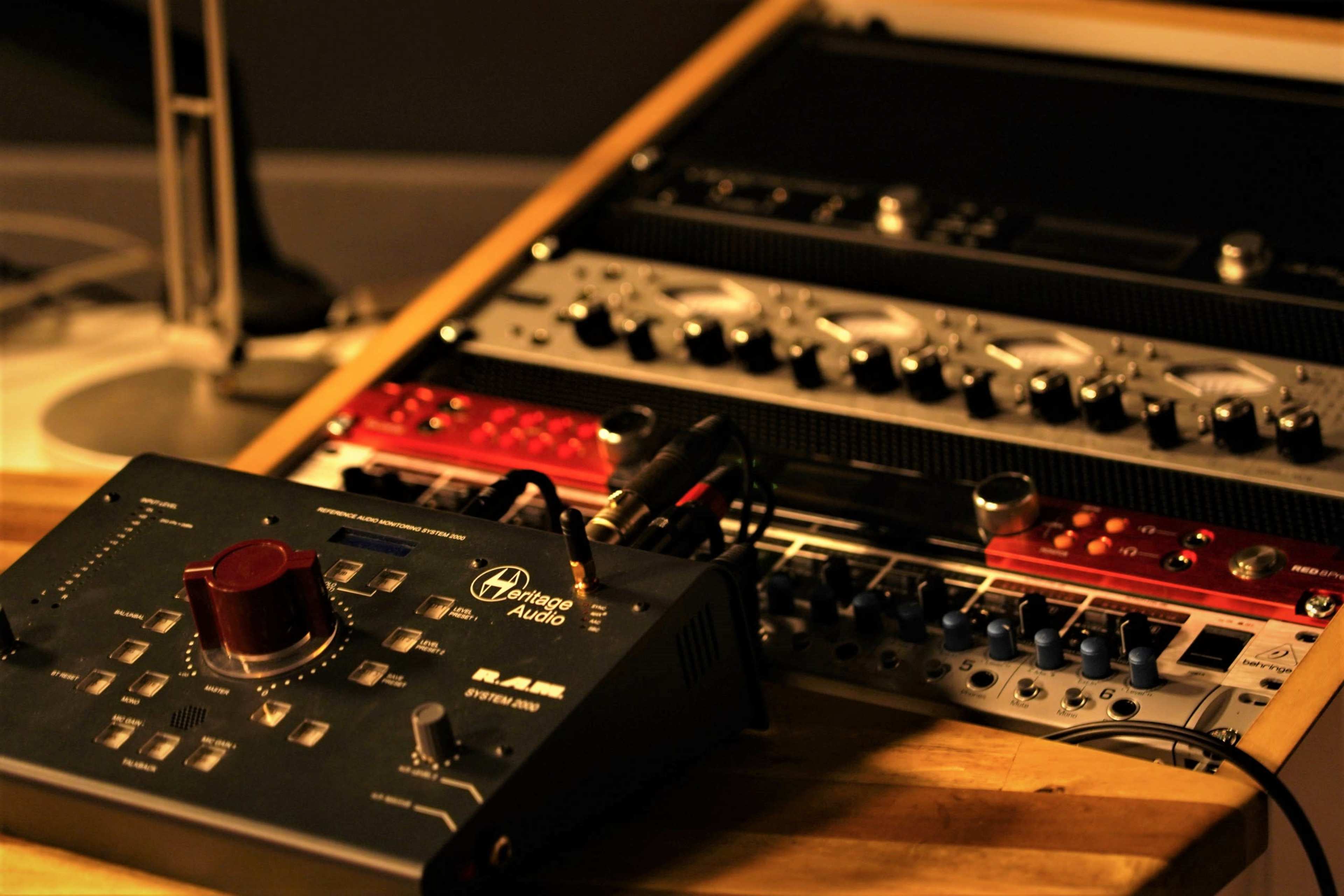 A collection of audio equipment, including a mixer and various rack-mounted devices, is arranged on a wooden surface.