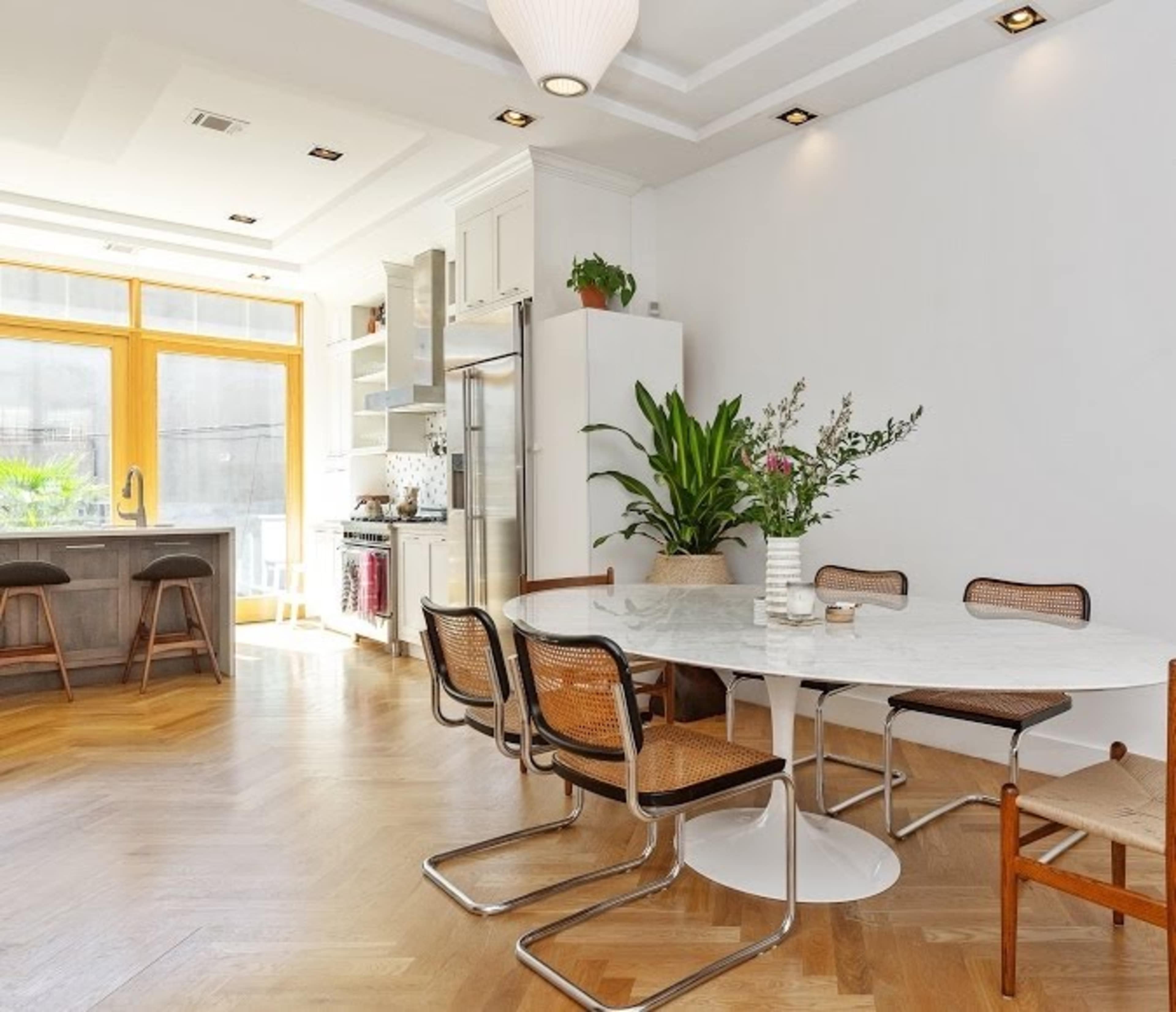A modern kitchen area features a round marble dining table surrounded by stylish chairs, with cabinets and appliances in a bright, open layout.