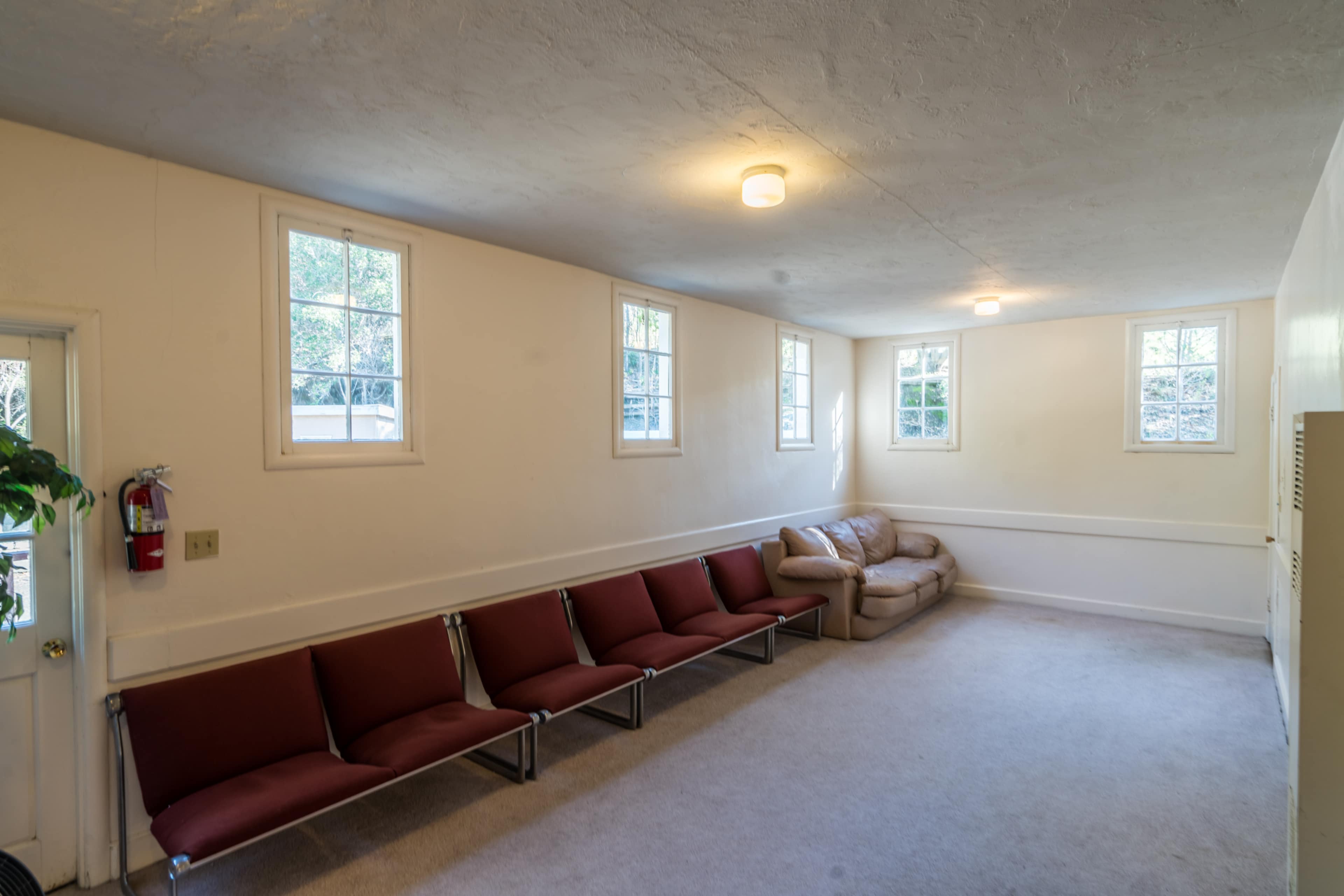 A clearly lit waiting room featuring a row of red chairs along one wall and a beige couch in the corner.