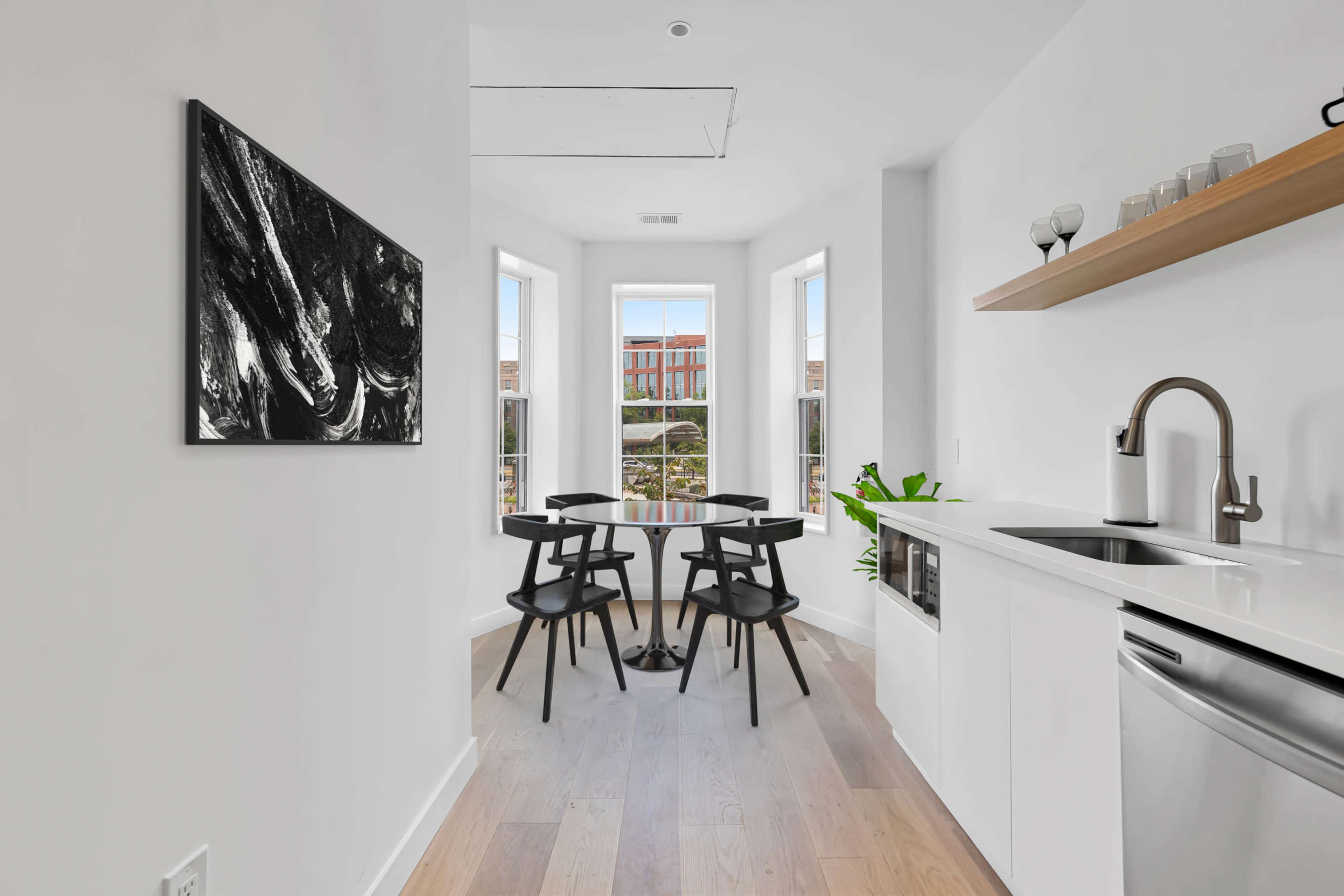A small dining area features a round table with four black chairs, surrounded by large windows and a sleek kitchen with modern appliances.