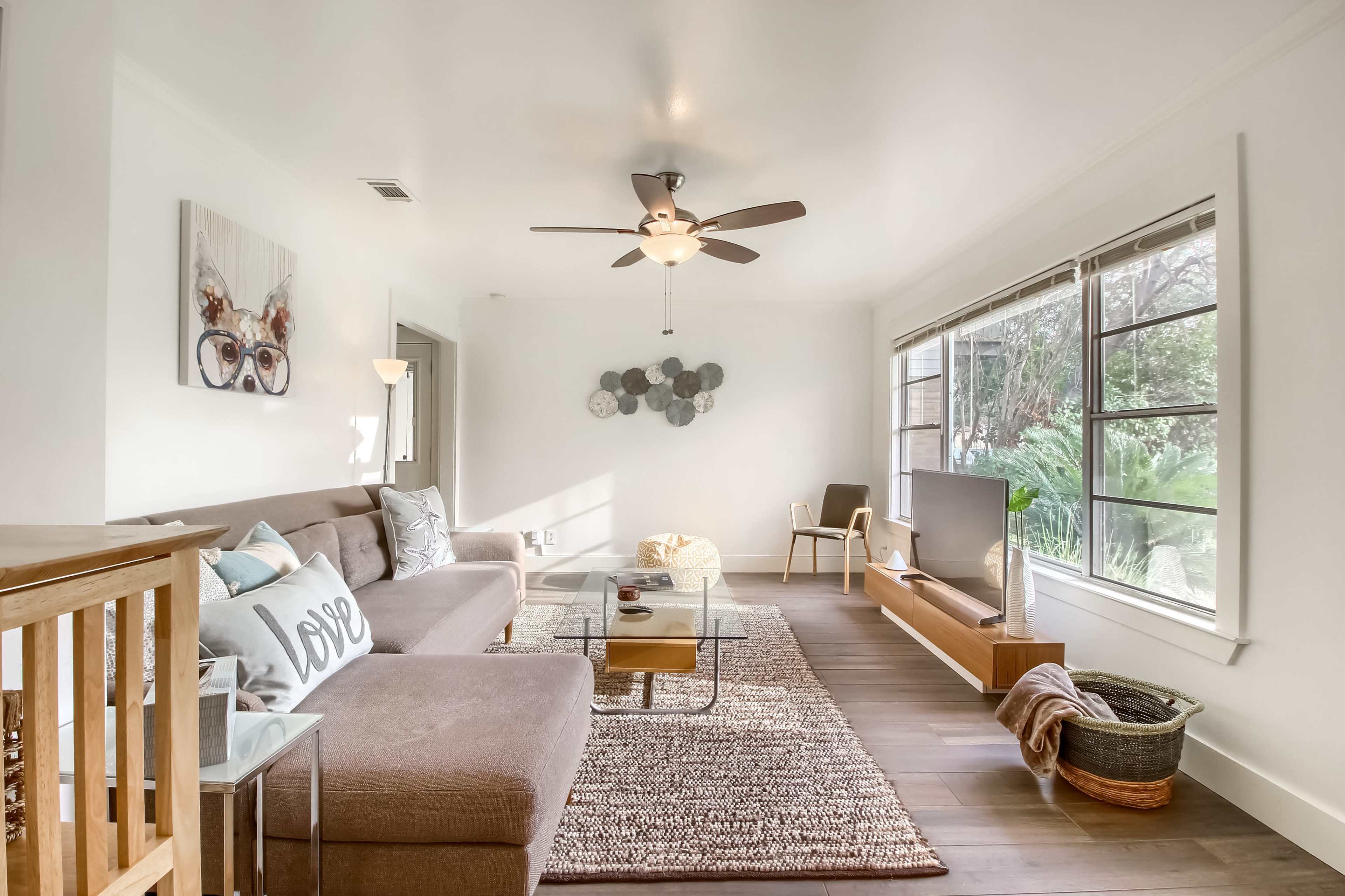 A bright, airy living room with a sectional sofa, a glass coffee table, and a large window overlooking greenery.
