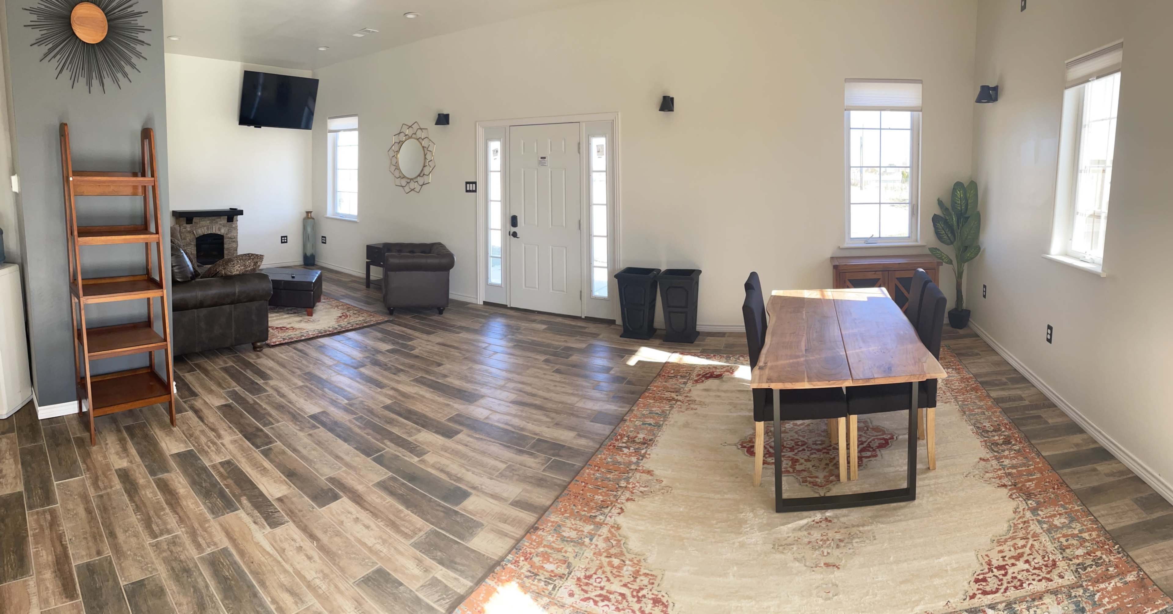 A spacious room with a wooden dining table, a couch, a small seating area, and large windows allowing natural light to enter.