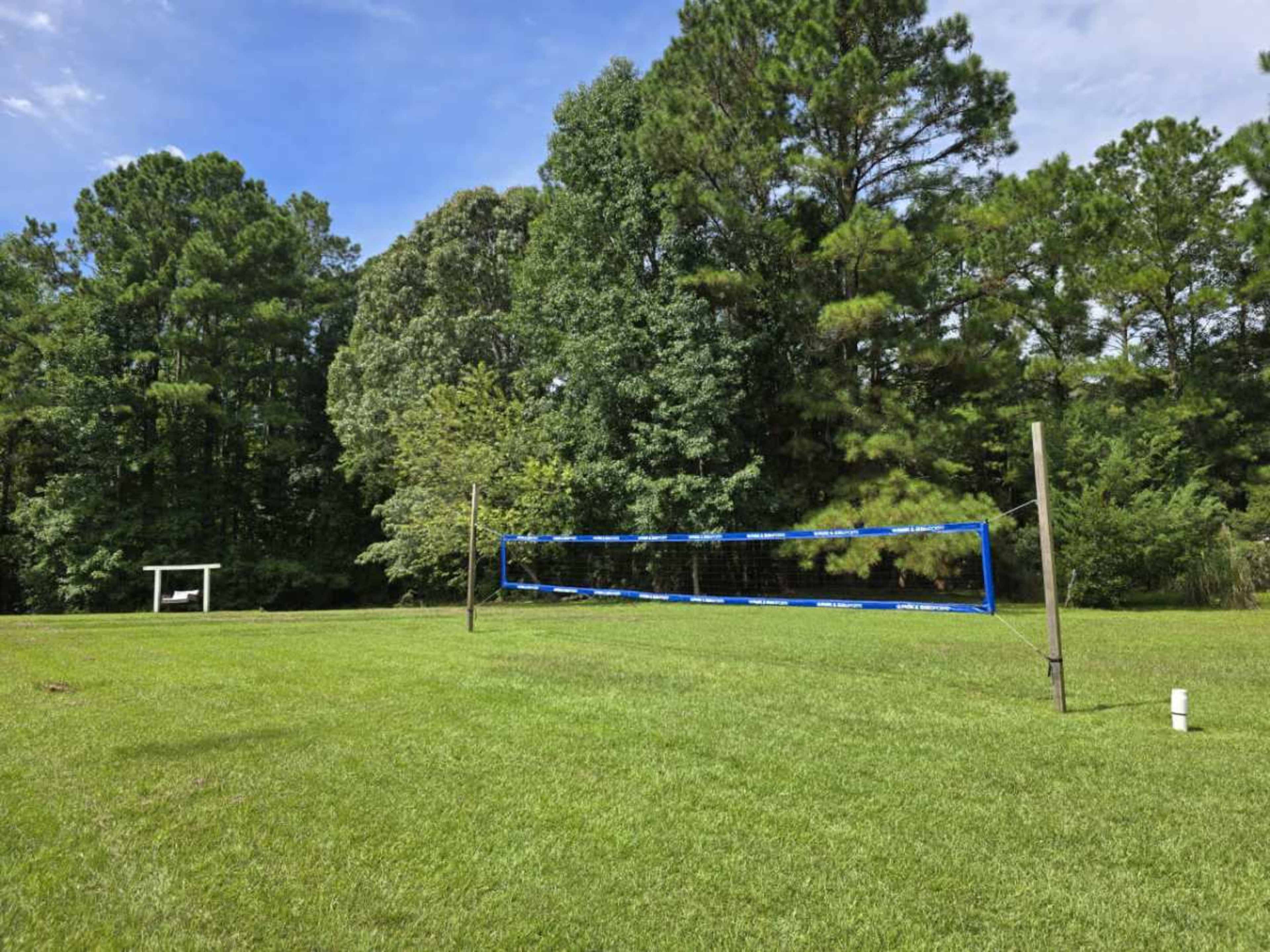 A volleyball net stands on a grassy area surrounded by trees.