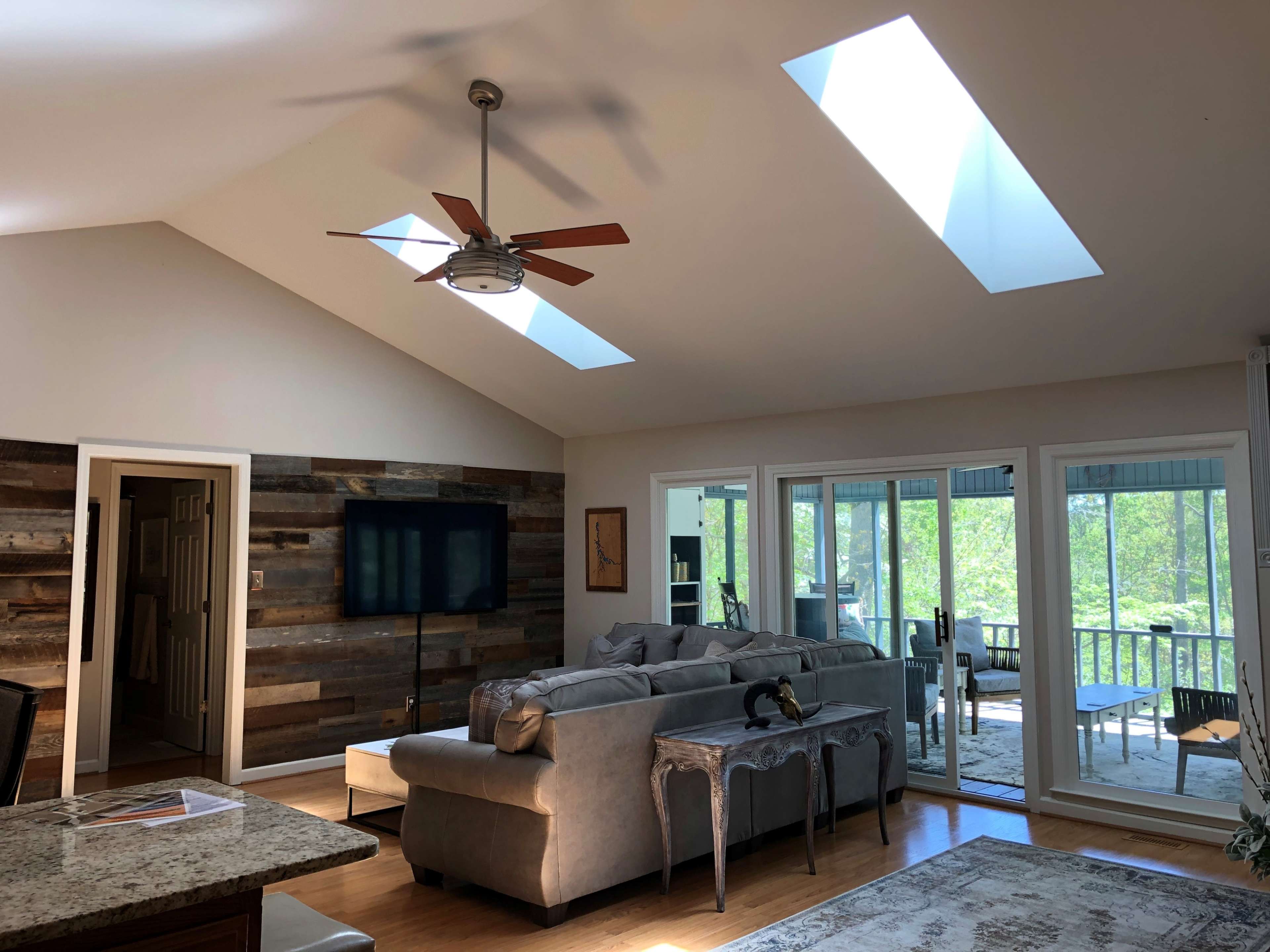 A modern living room with a vaulted ceiling, skylights, a sectional sofa, and large windows overlooking a patio.