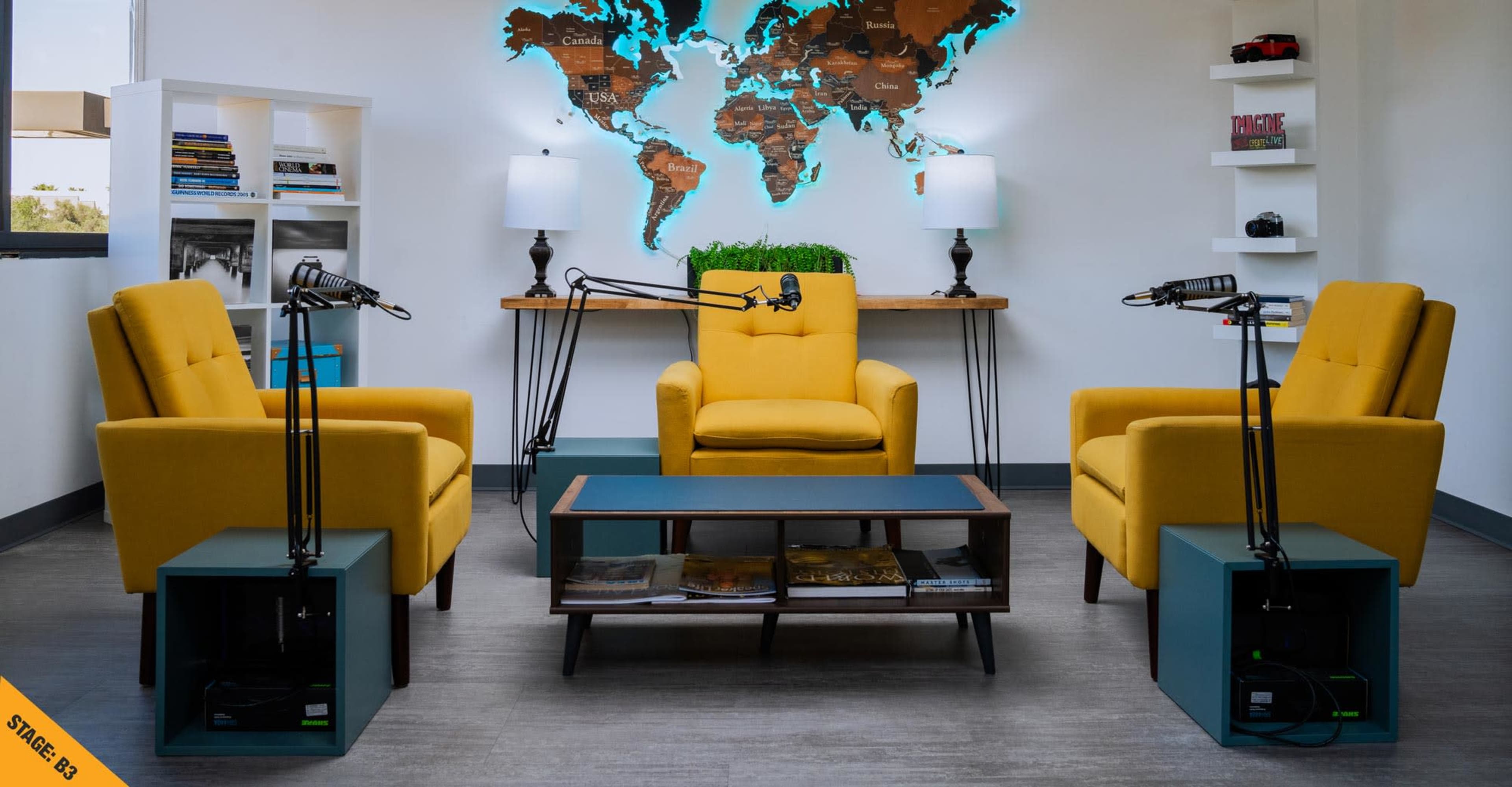 A modern podcasting studio features three yellow chairs, a coffee table, and a world map on the wall, with microphones set up for recording.
