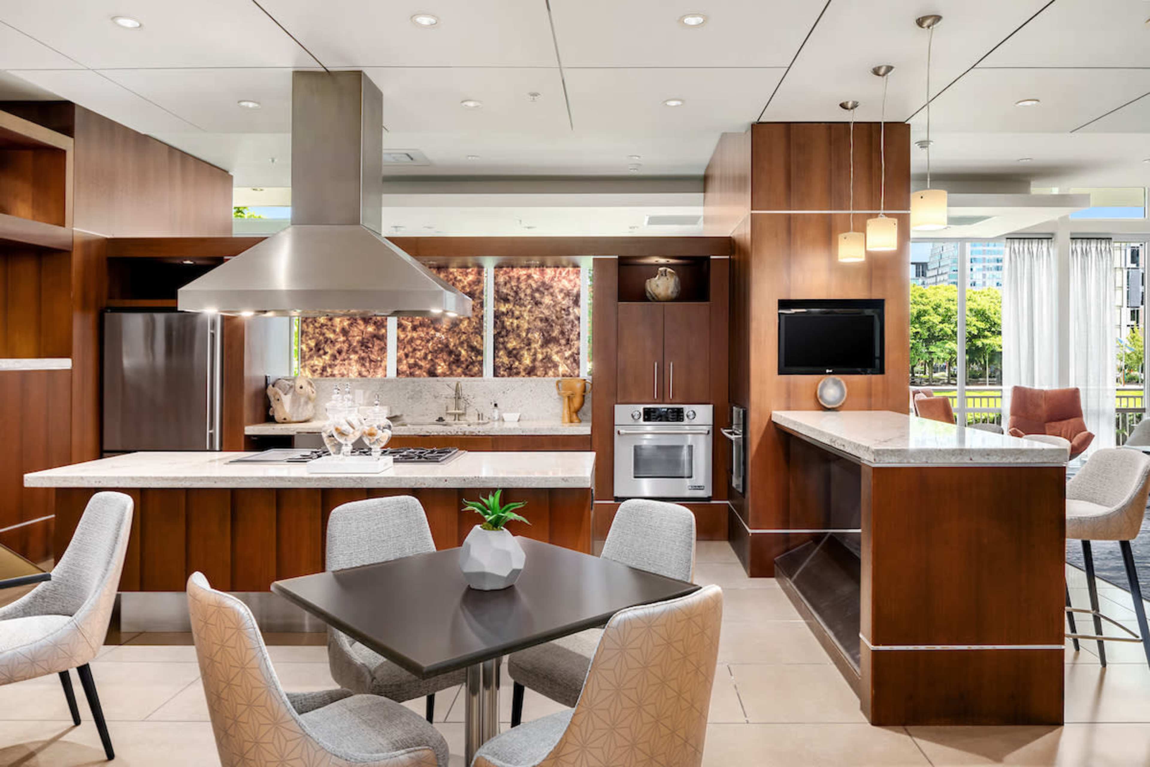 A modern kitchen with stainless steel appliances, wooden cabinetry, and a dining area featuring a table and upholstered chairs.