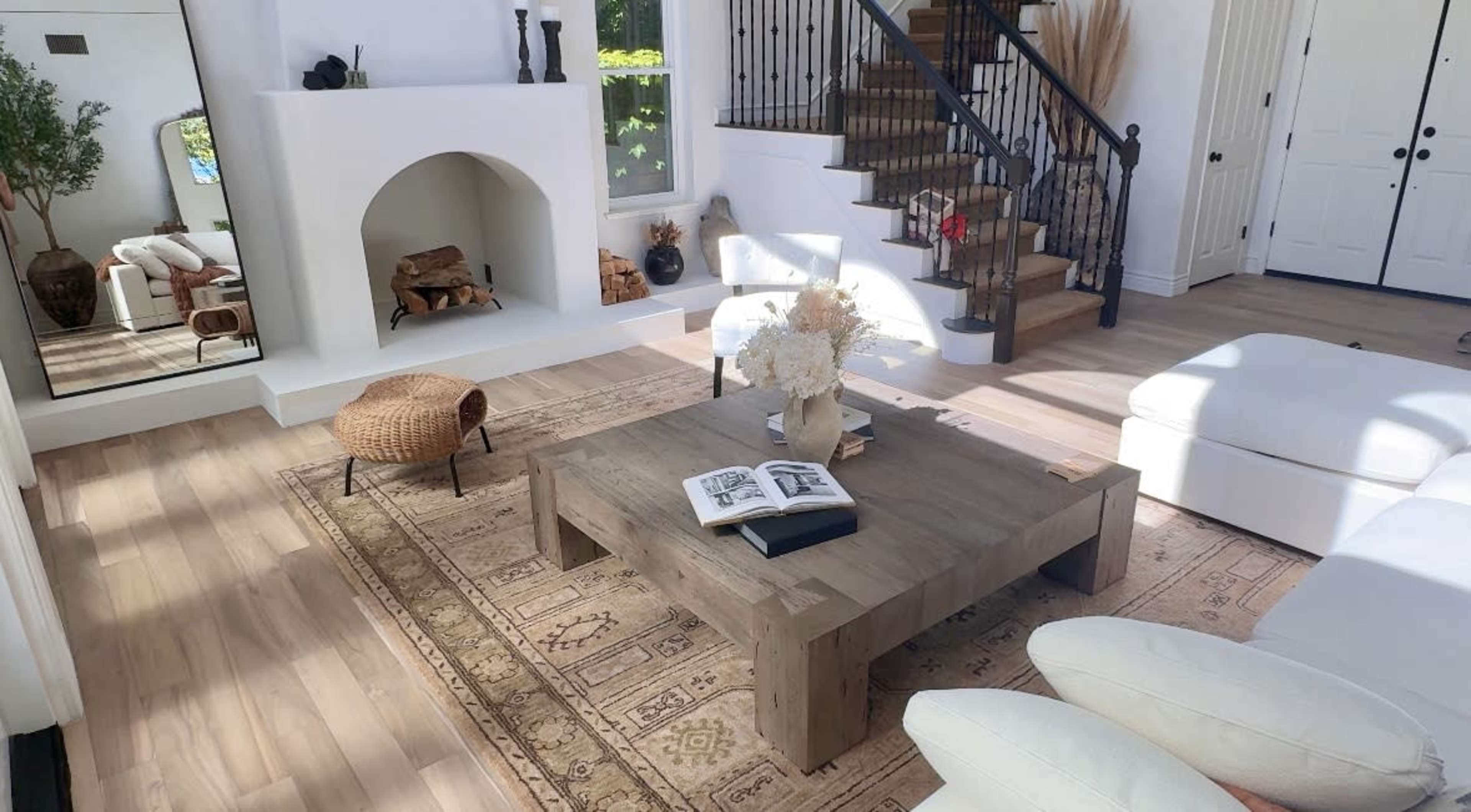 A modern living room featuring a white sofa, a wooden coffee table with an open book, a decorative rug, and a staircase with a black railing.