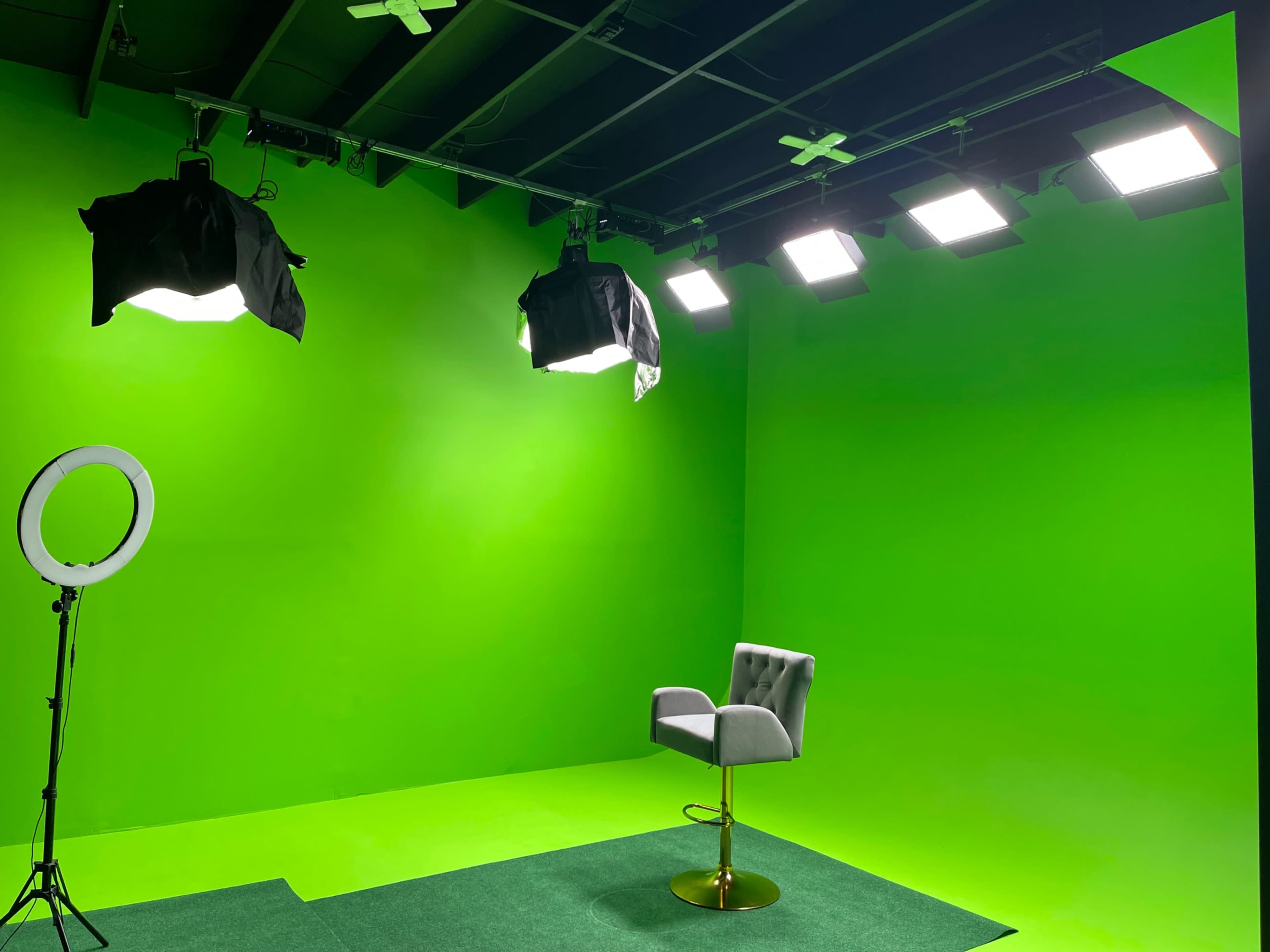 A green screen studio setup with a single chair, bright lighting, and a ring light on a stand.
