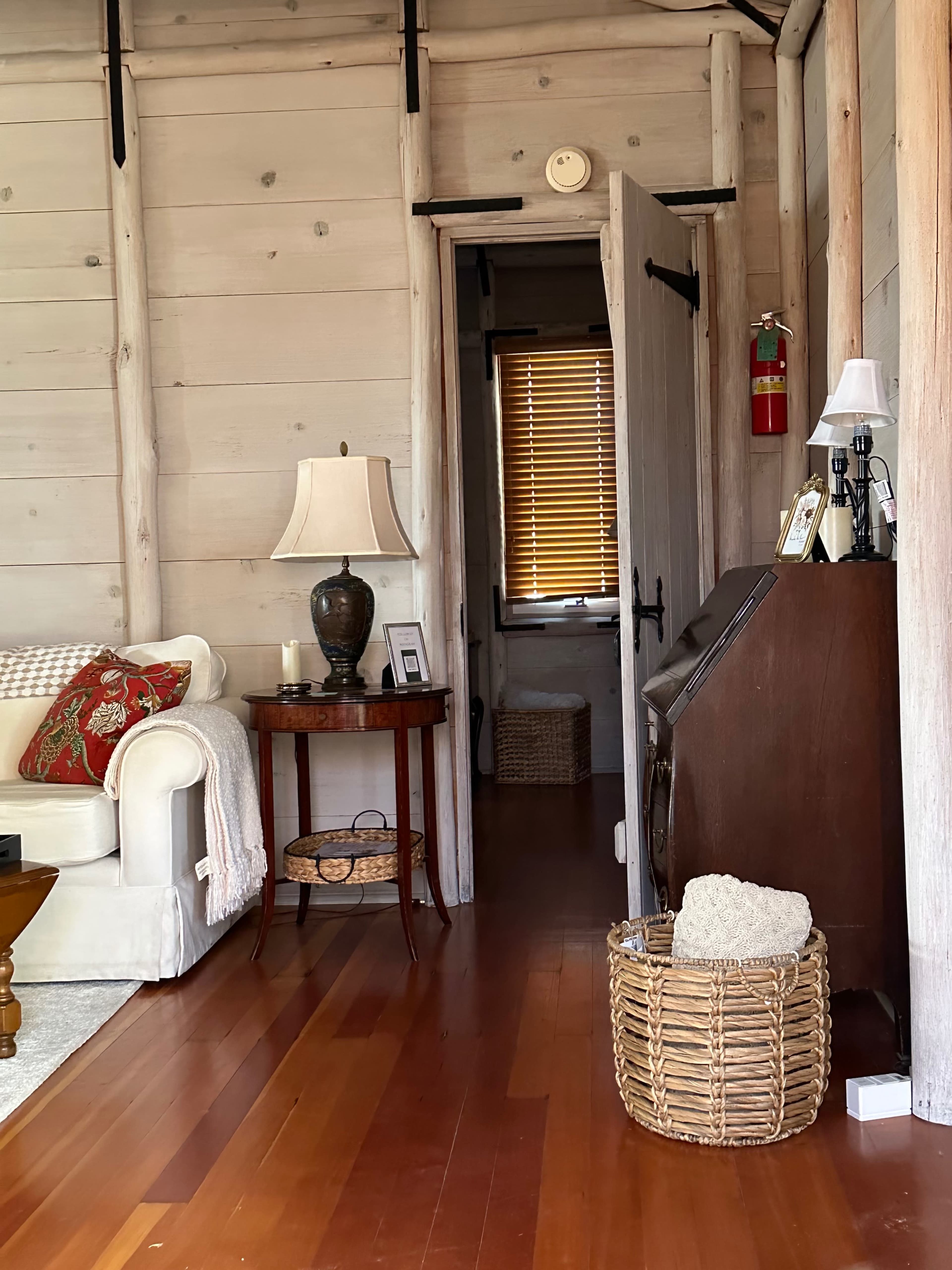 A cozy interior with a living room featuring a white sofa and a table, leading into a hallway with a door and wooden accents.