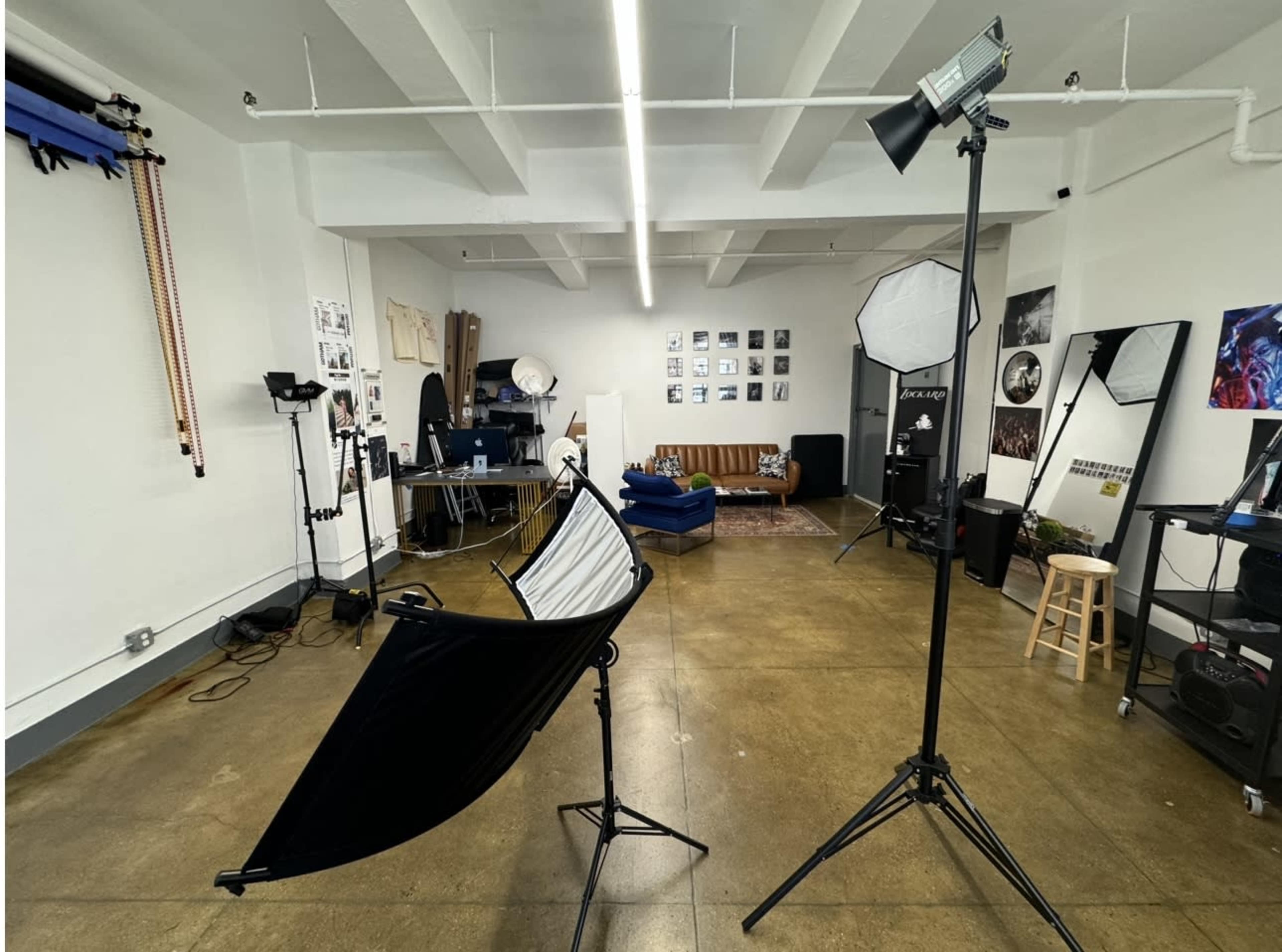 A photography studio with various equipment, including lighting setups, a brown sofa, and framed photographs on the walls.