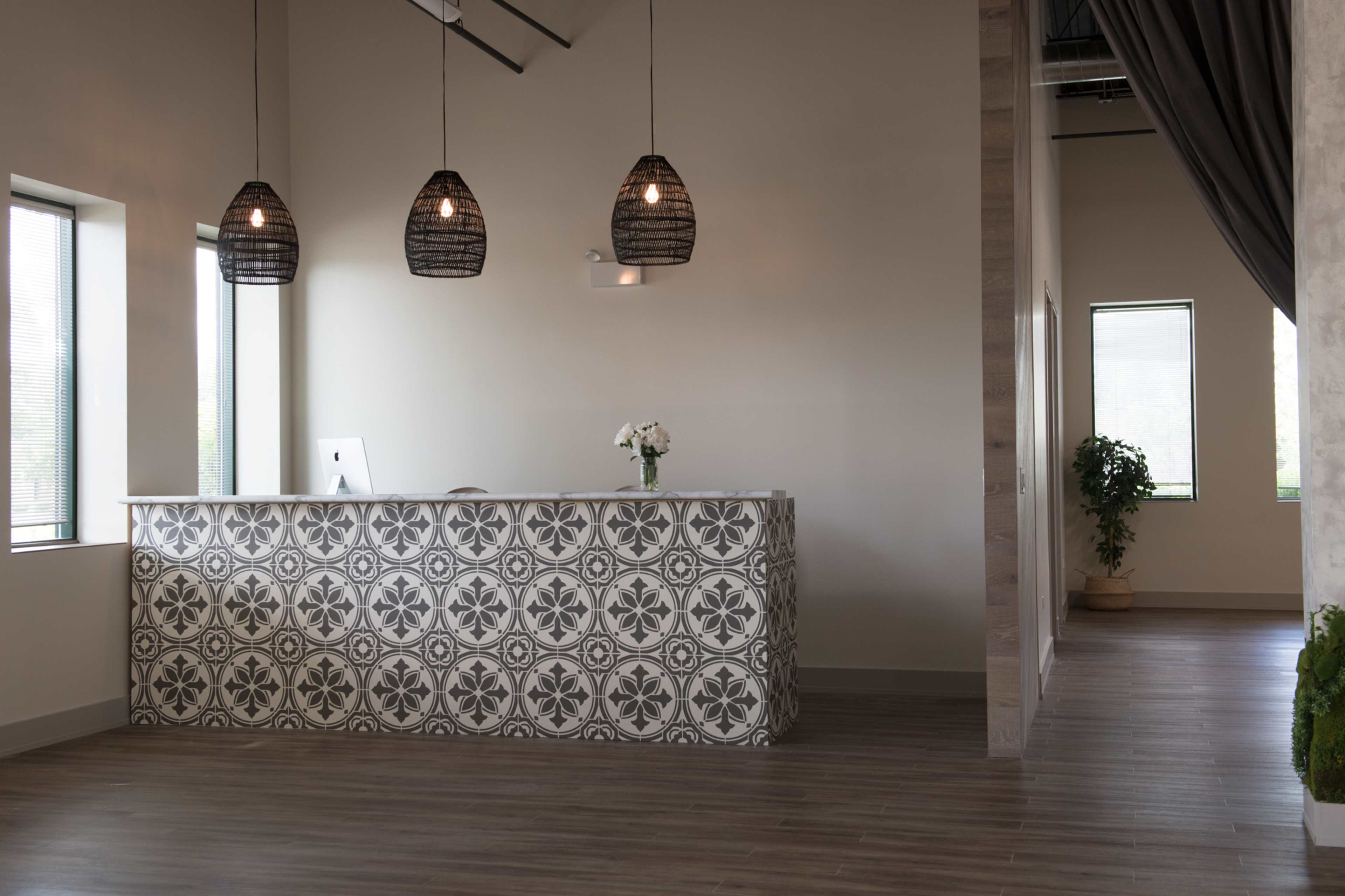 A modern reception area featuring a patterned desk, large windows, and pendant lighting.