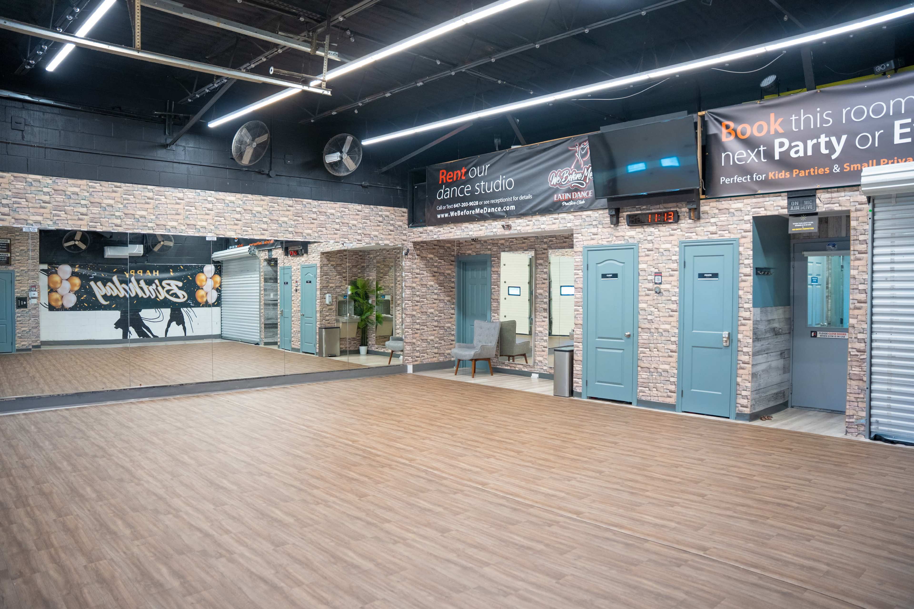 The image shows an empty dance studio with wooden flooring, mirrored walls, and a wall featuring a banner for room rental.