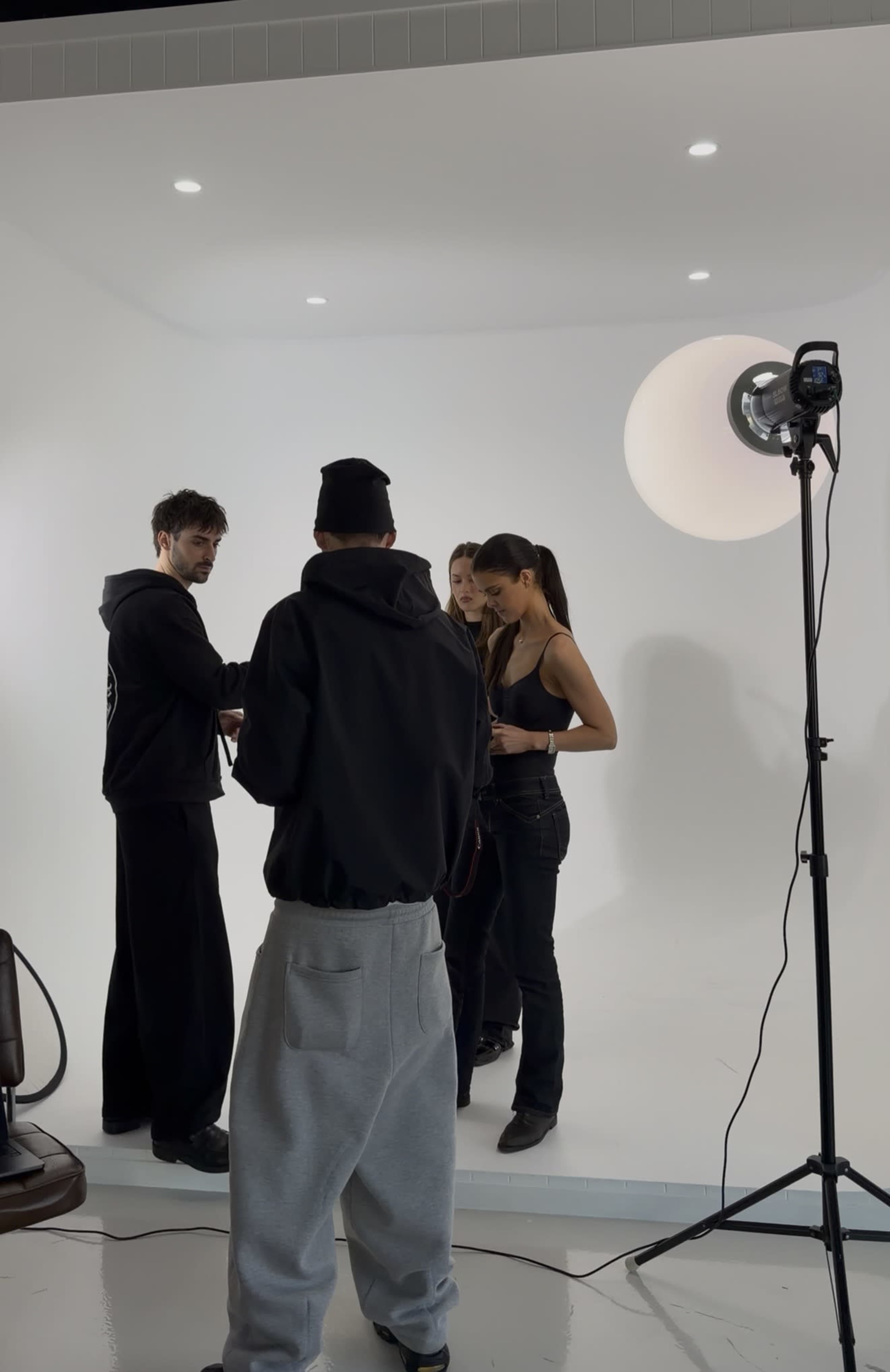 A group of four people is discussing in a photo studio that has a plain white backdrop and a lighting setup.