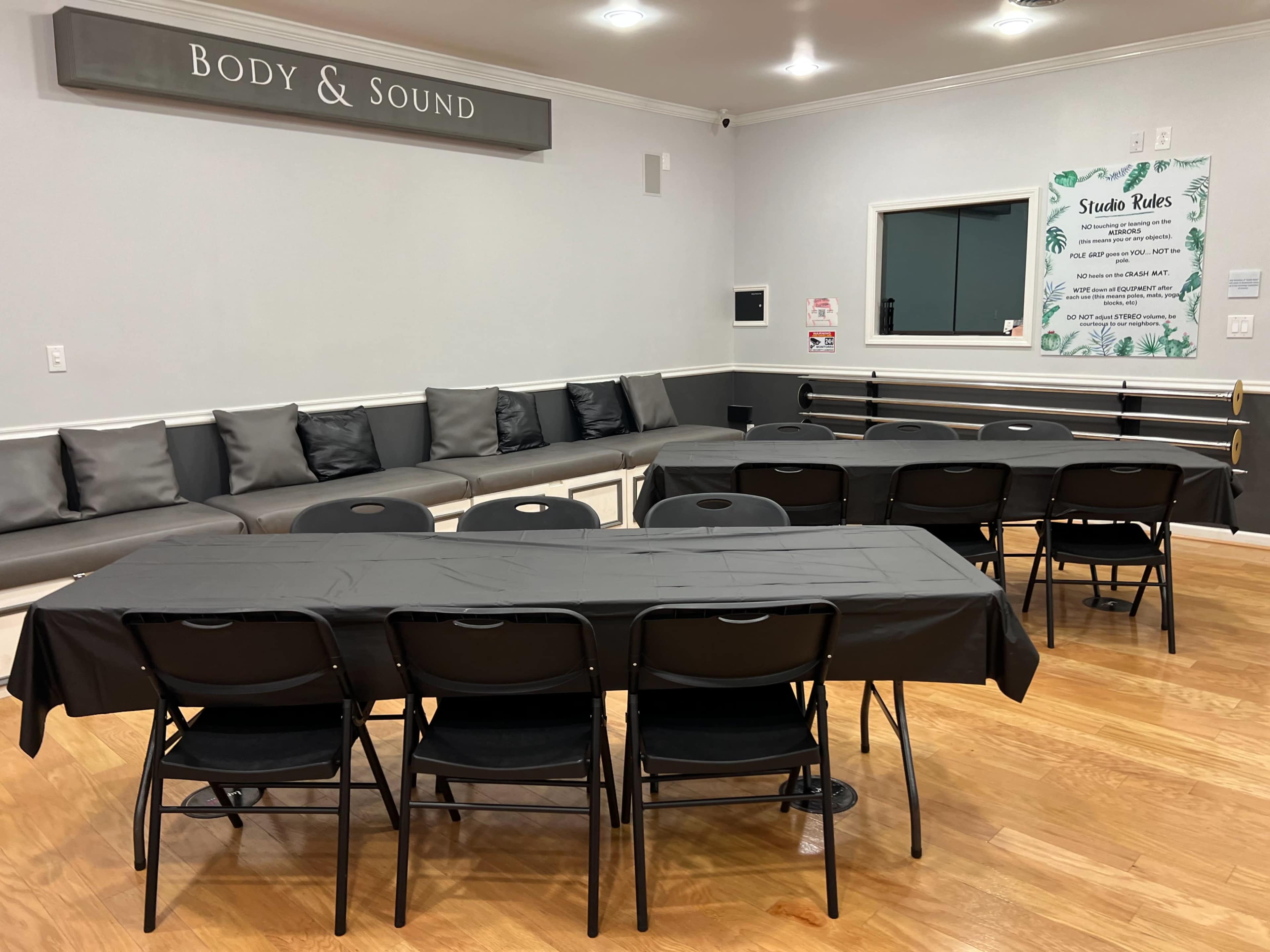 A room with a row of black folding chairs and tables arranged for an event, with a sign reading "Body & Sound" on the wall and a list of studio rules displayed nearby.
