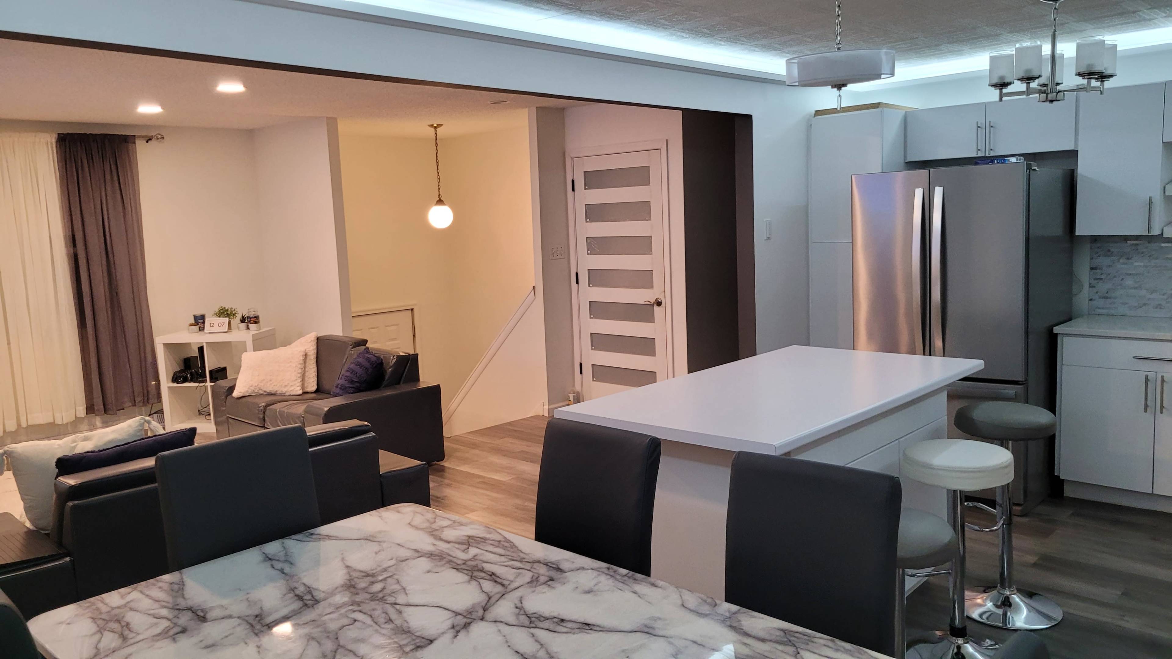 A modern kitchen and dining area with an island, sleek appliances, and a view into a living space featuring a couch and decorative lighting.