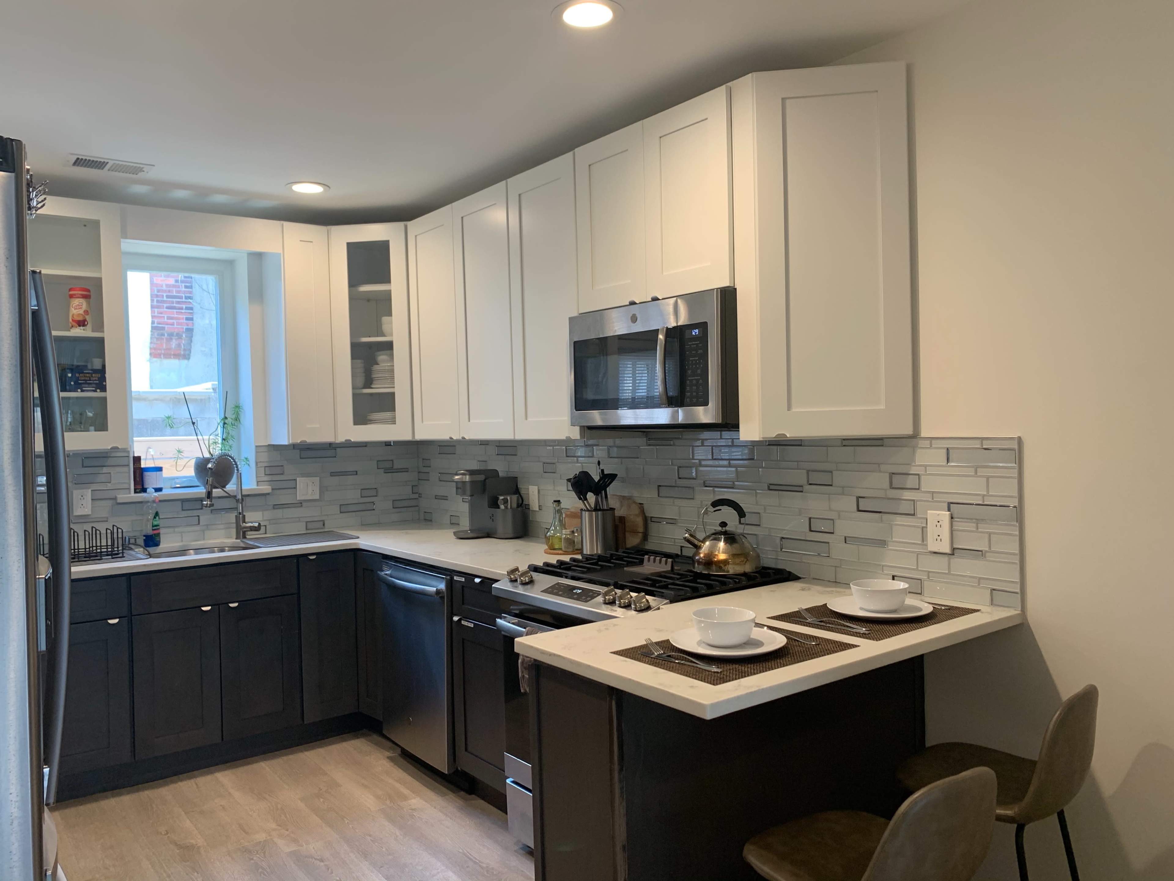 The image shows a modern kitchen with white cabinets, stainless steel appliances, and a countertop with two place settings.