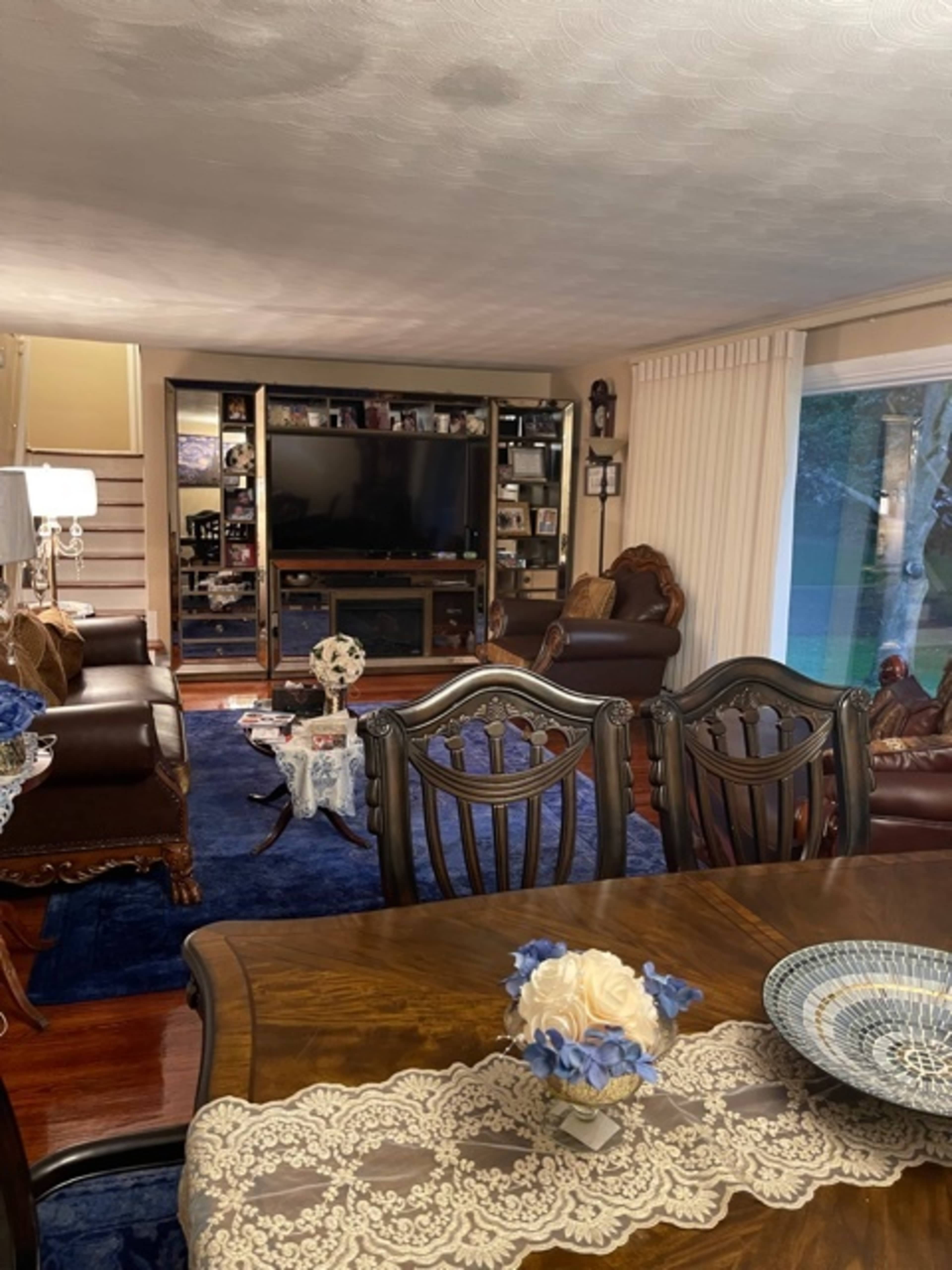 The room features a living area with brown leather furniture, a large television, and a dining table set with decorative items.