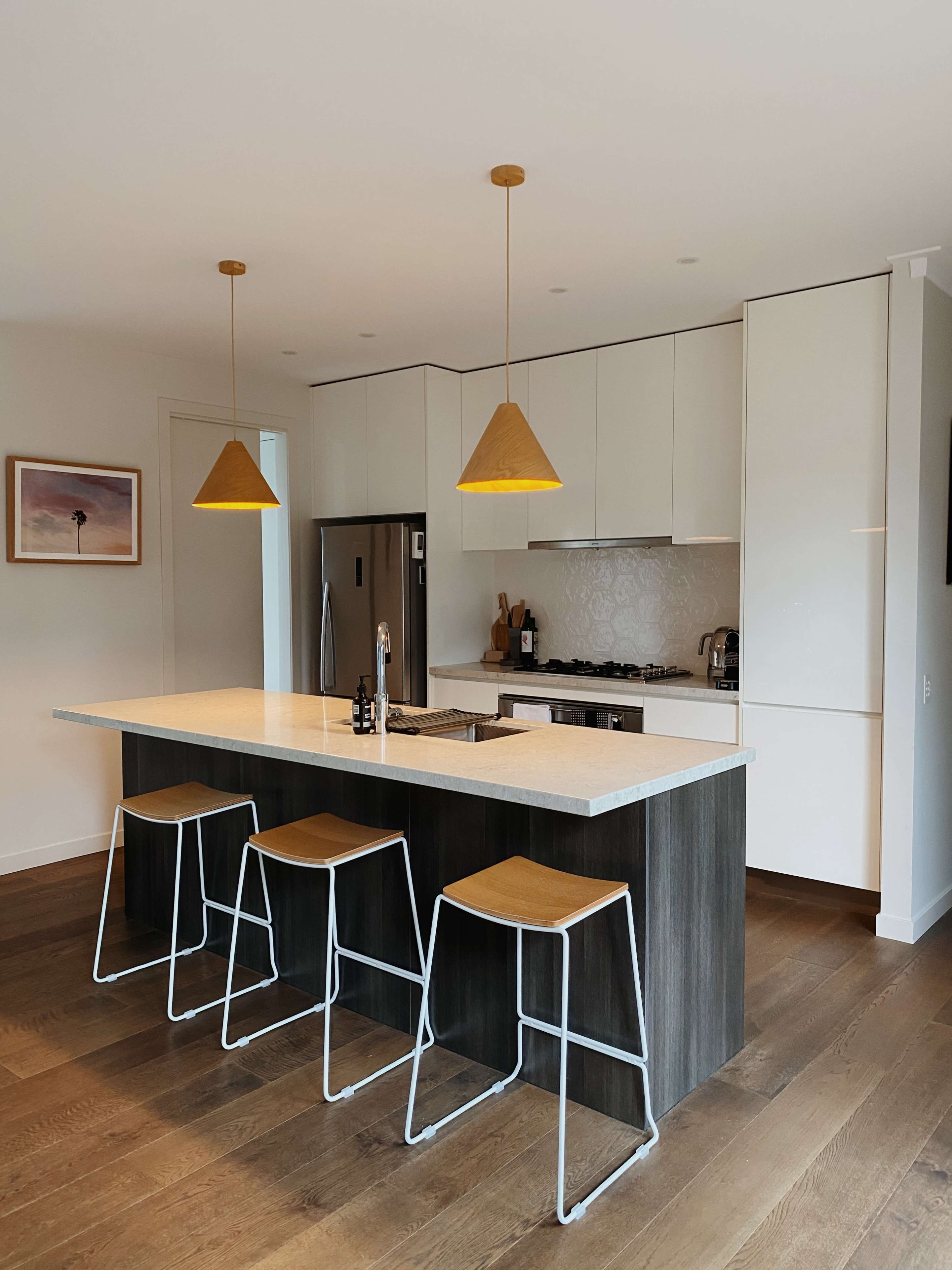 A modern kitchen with a central island, three bar stools, and pendant lights hanging overhead.