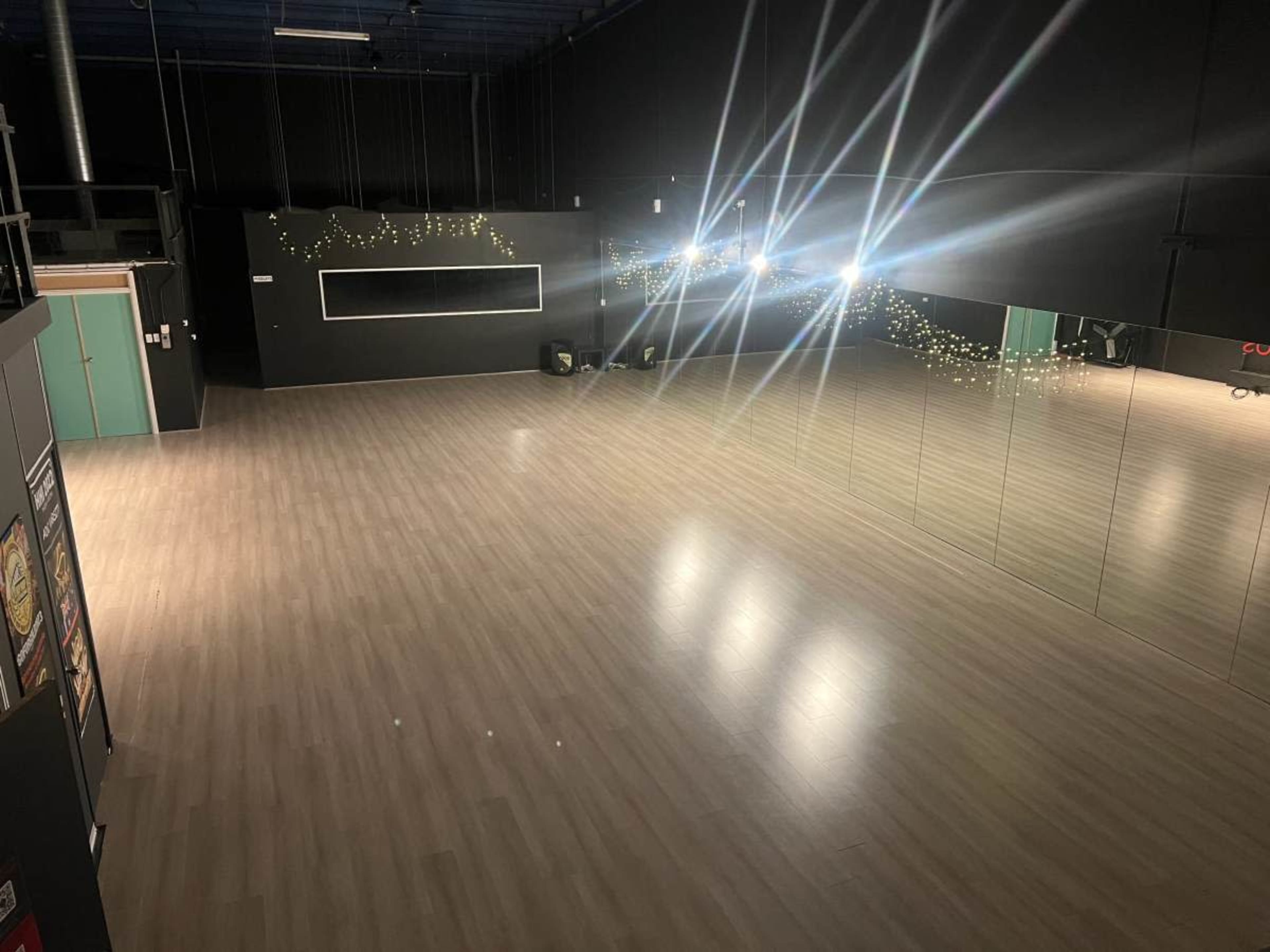 The image depicts an empty dance studio with wooden flooring and a large mirror on one wall, illuminated by scattered lights.