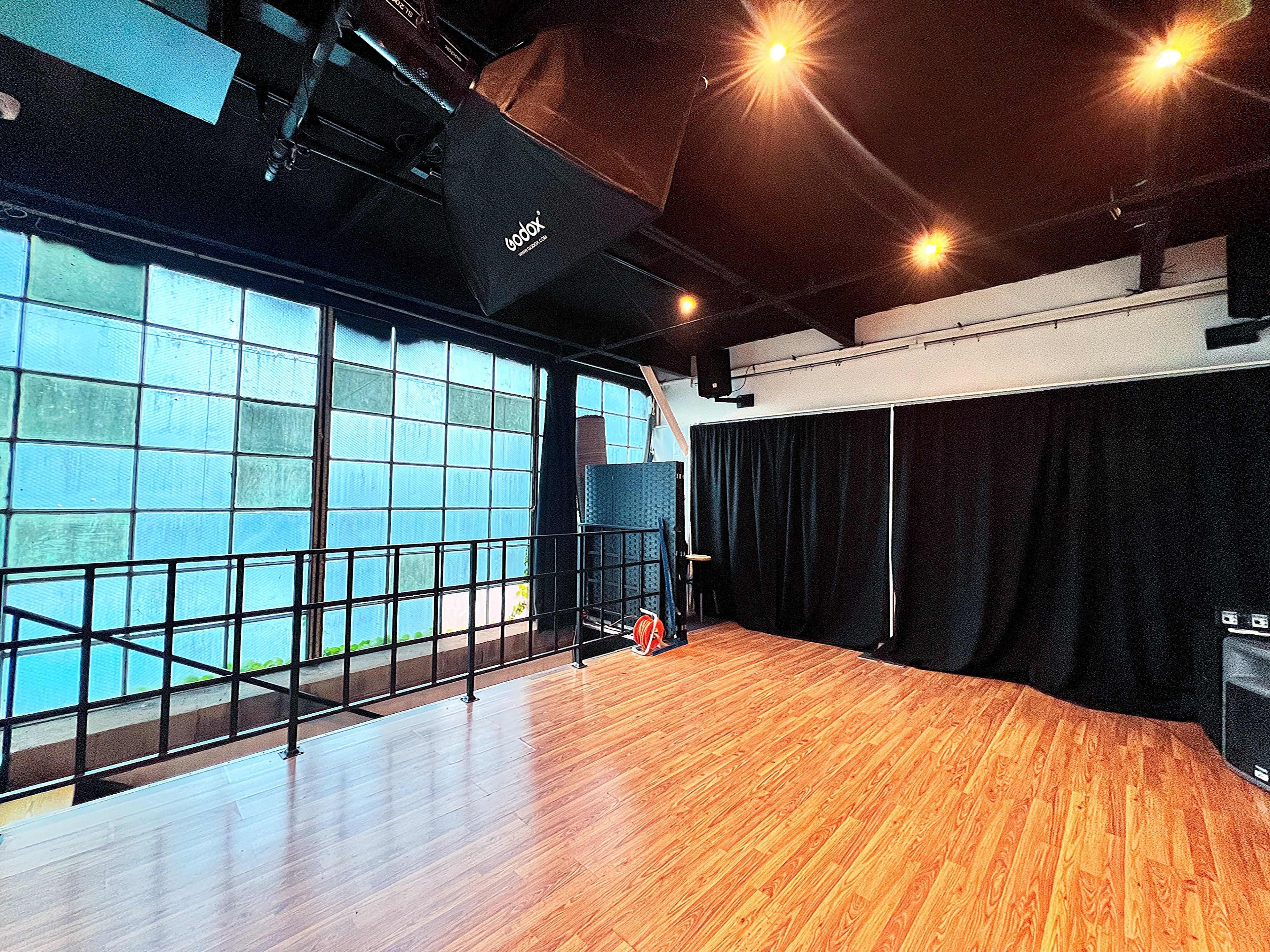 A spacious room with wooden flooring, large windows, and a black curtain along one side.