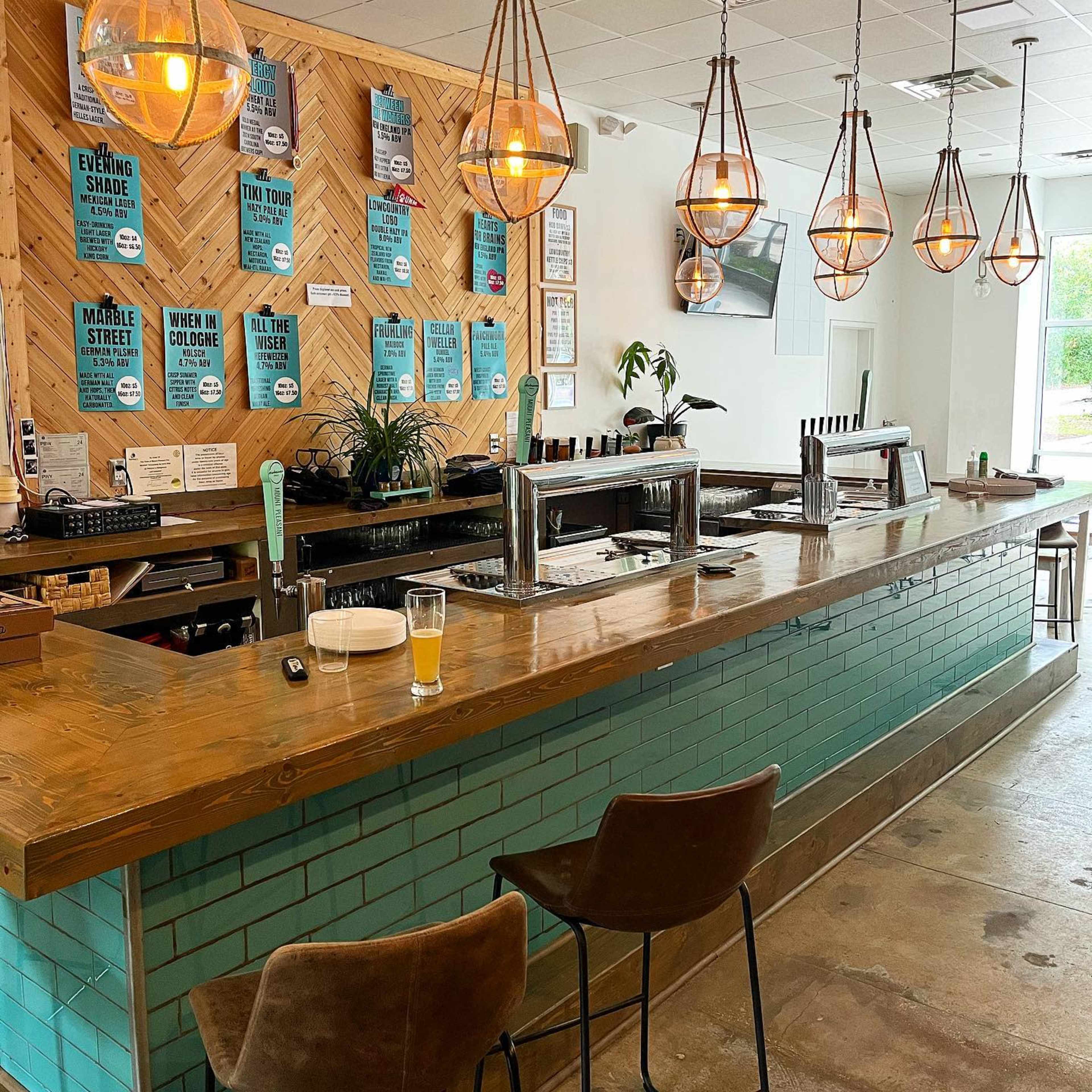 A modern bar area features a wooden countertop with turquoise tiles, hanging pendant lights, and promotional posters on the wall.