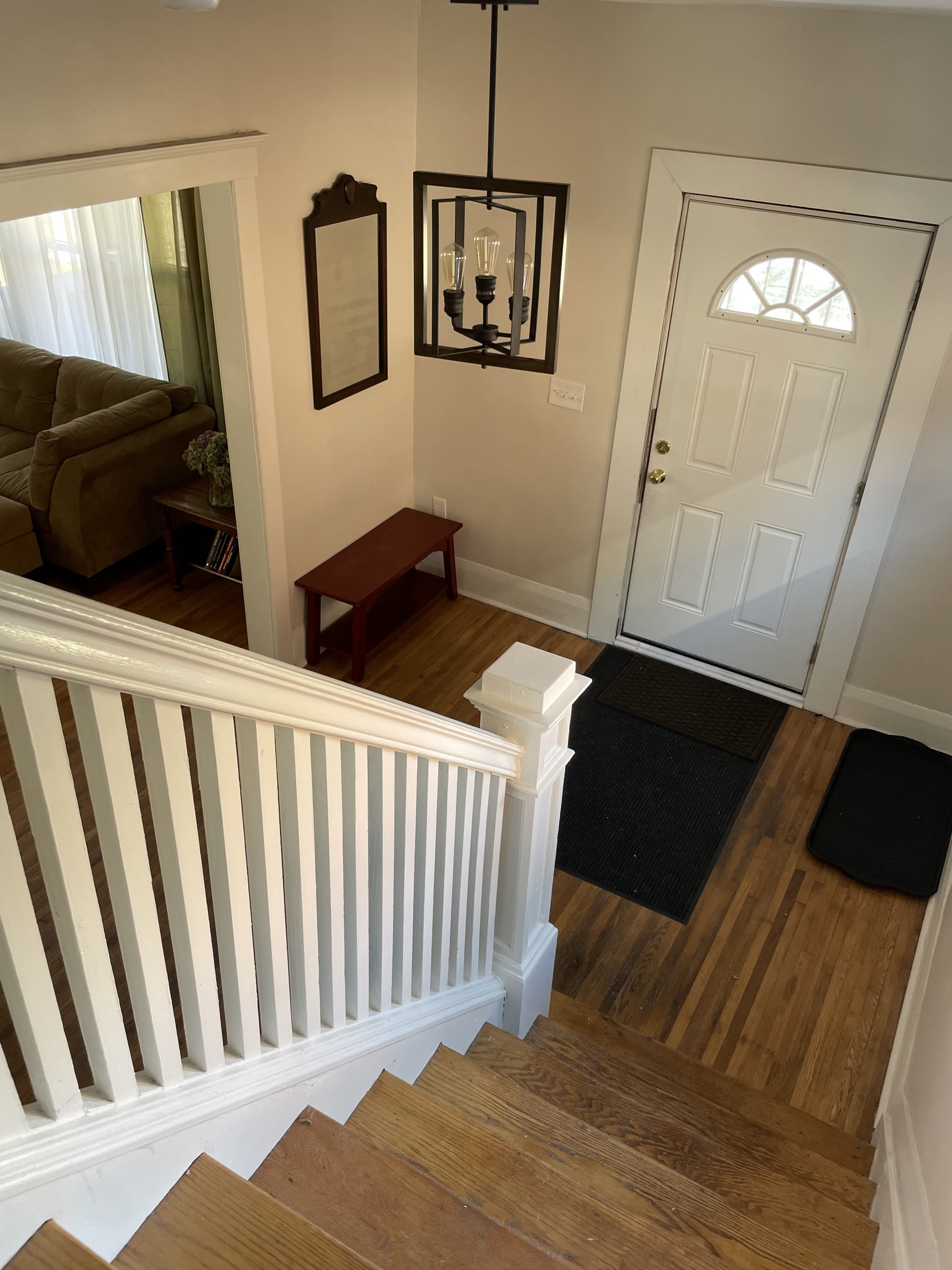 A well-lit entryway with a staircase, a door with a window, a small table, and a black mat on the wooden floor.