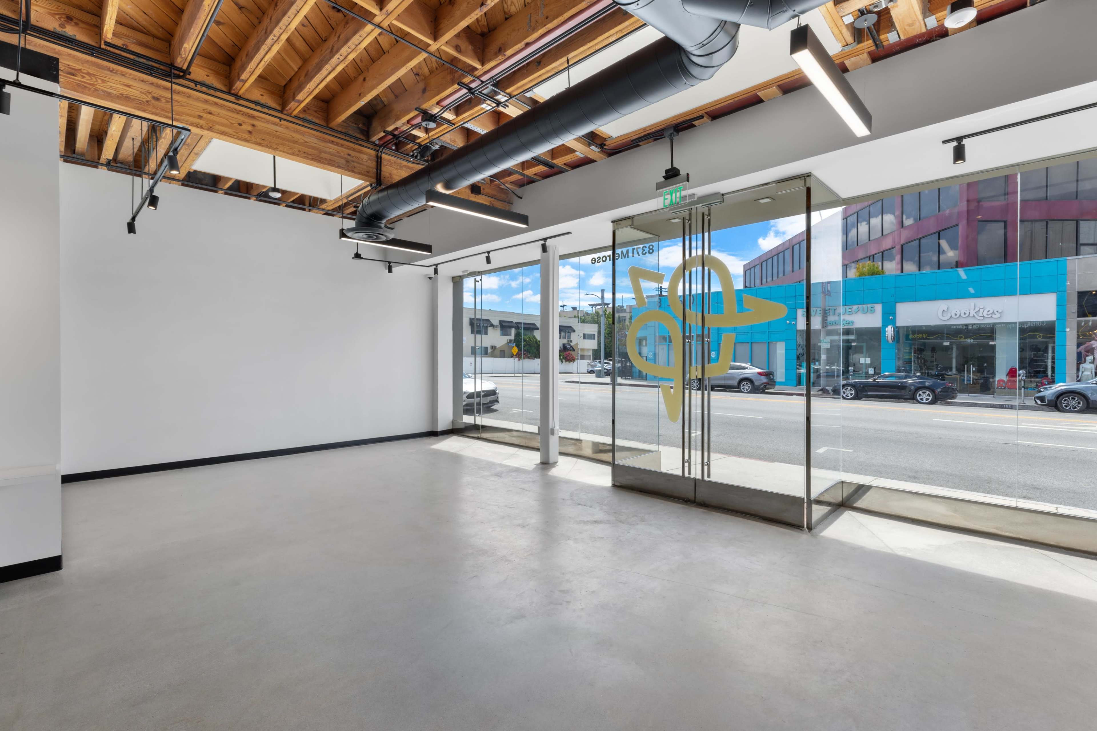 An empty commercial space with large glass doors leading to a street view, featuring exposed wooden beams on the ceiling.