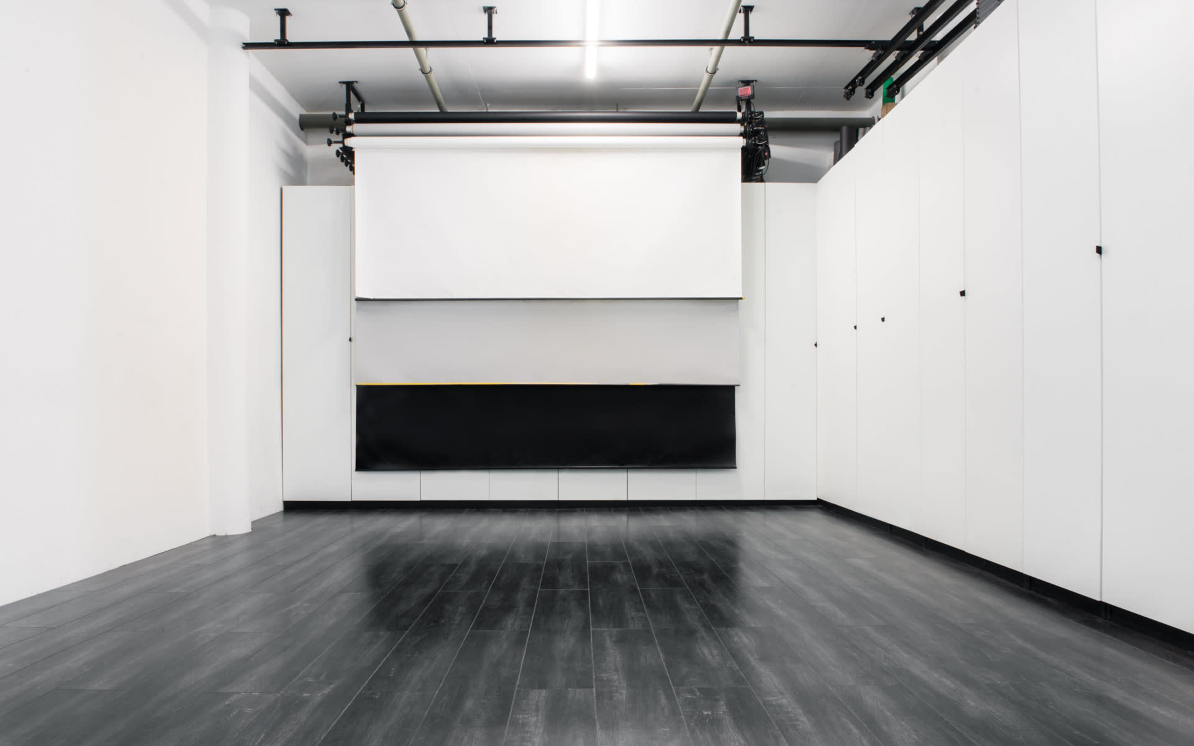 A spacious, empty room with white walls, dark flooring, and a retractable screen mounted on the ceiling.