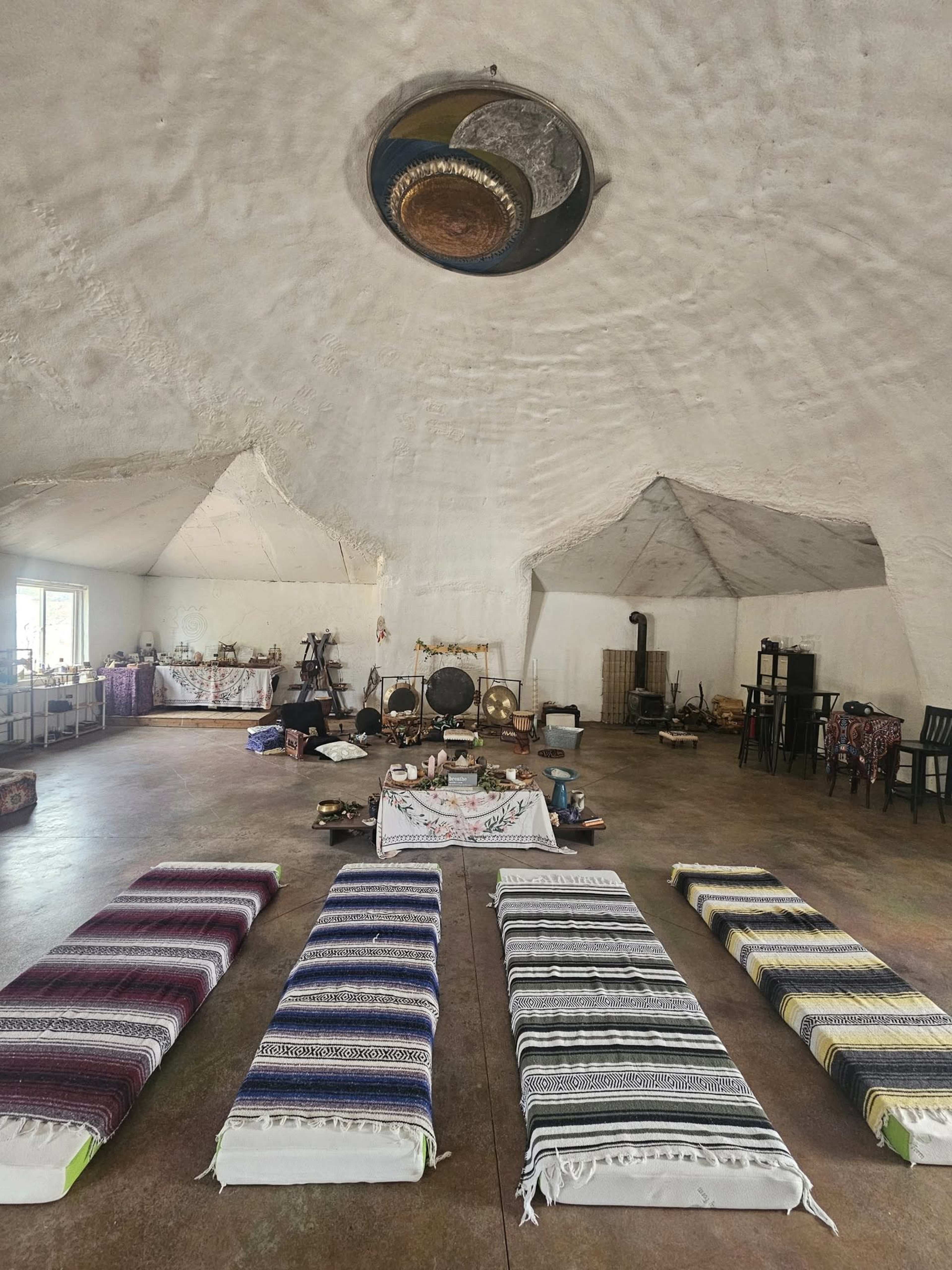 The interior of a spacious, circular room features several woven mats arranged in rows on the floor, surrounded by various instruments and decor items.