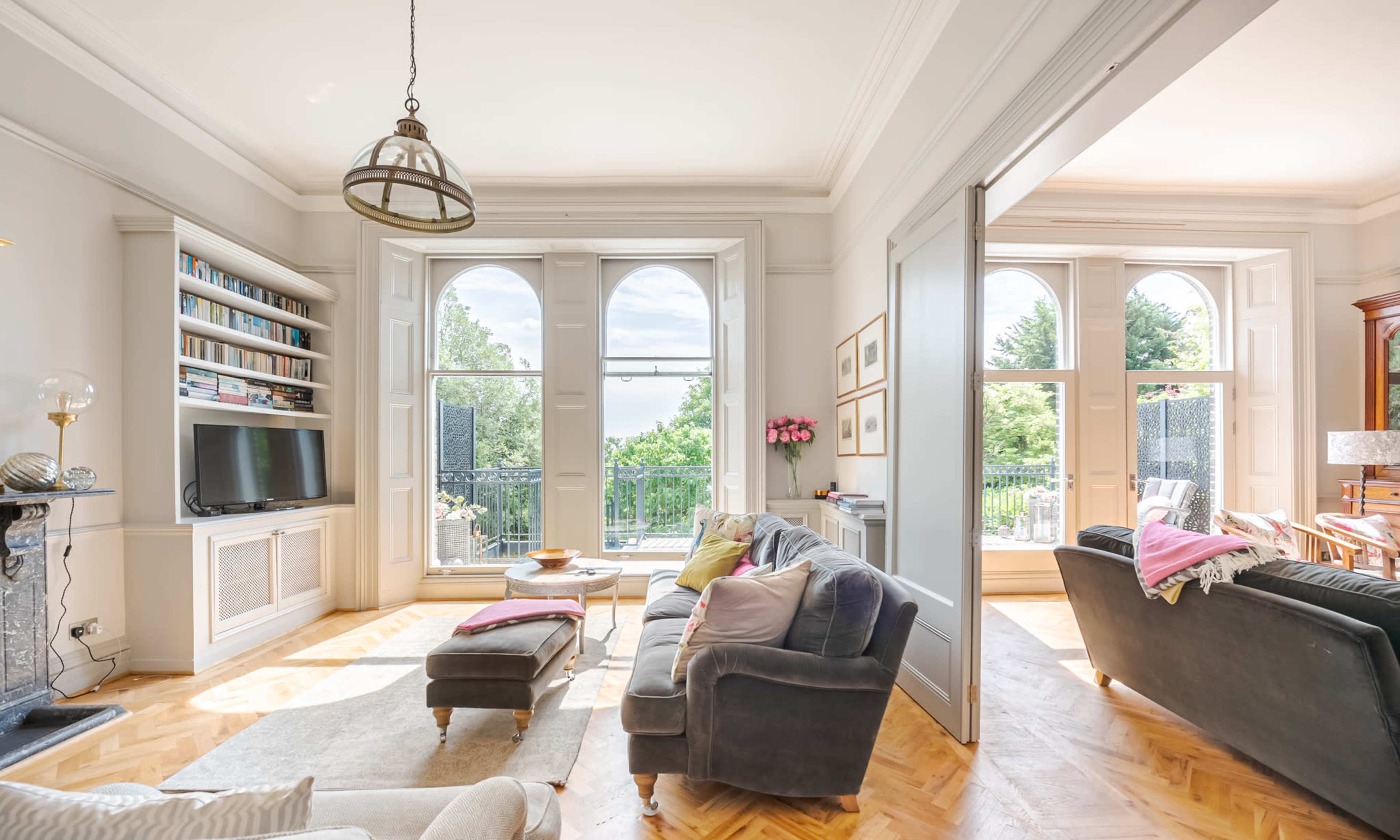 A spacious living room features large arched windows, a television unit, and comfortable seating arranged around a coffee table.
