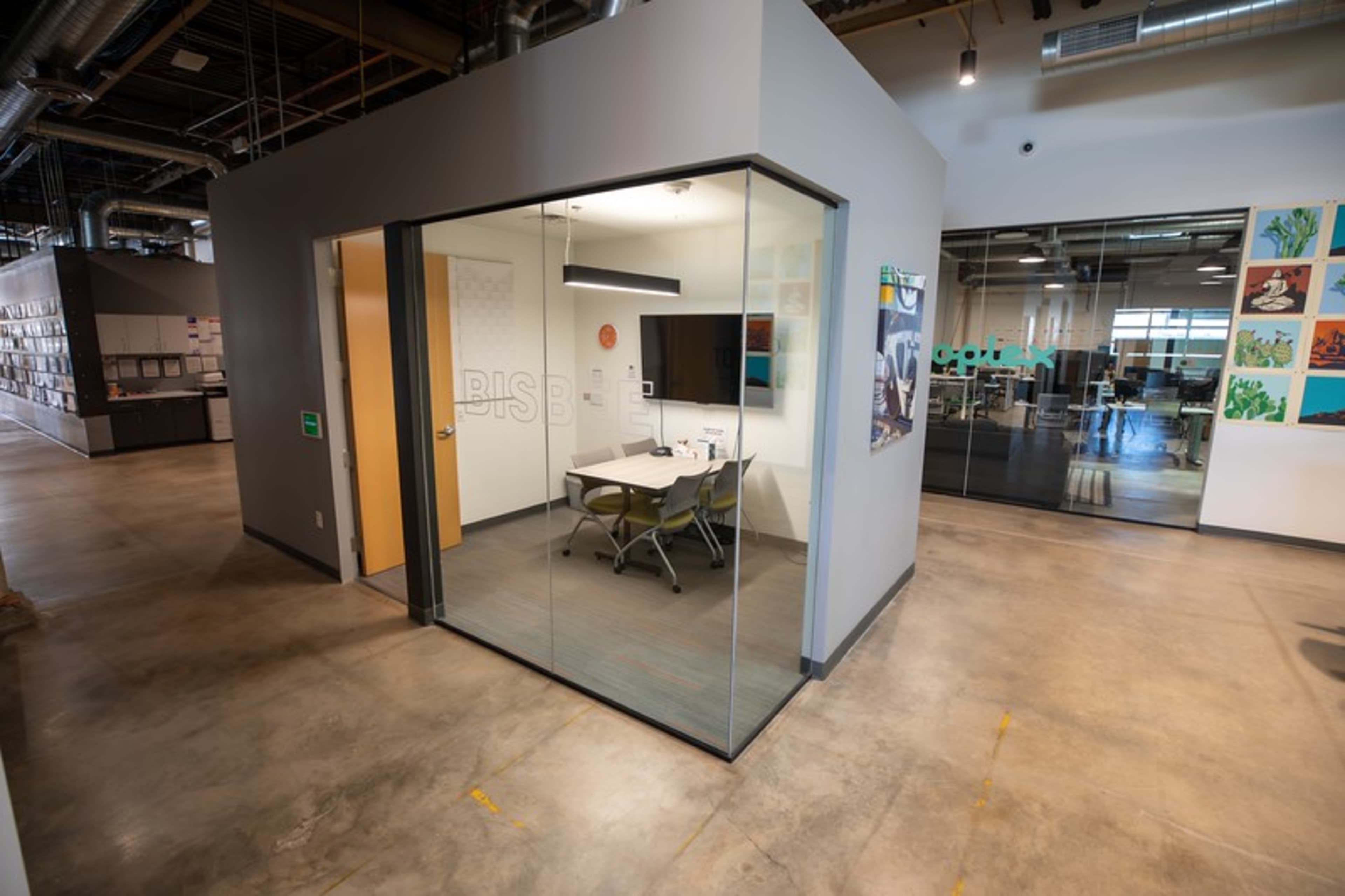 A modern office space with a glass-walled meeting room featuring a table and chairs.