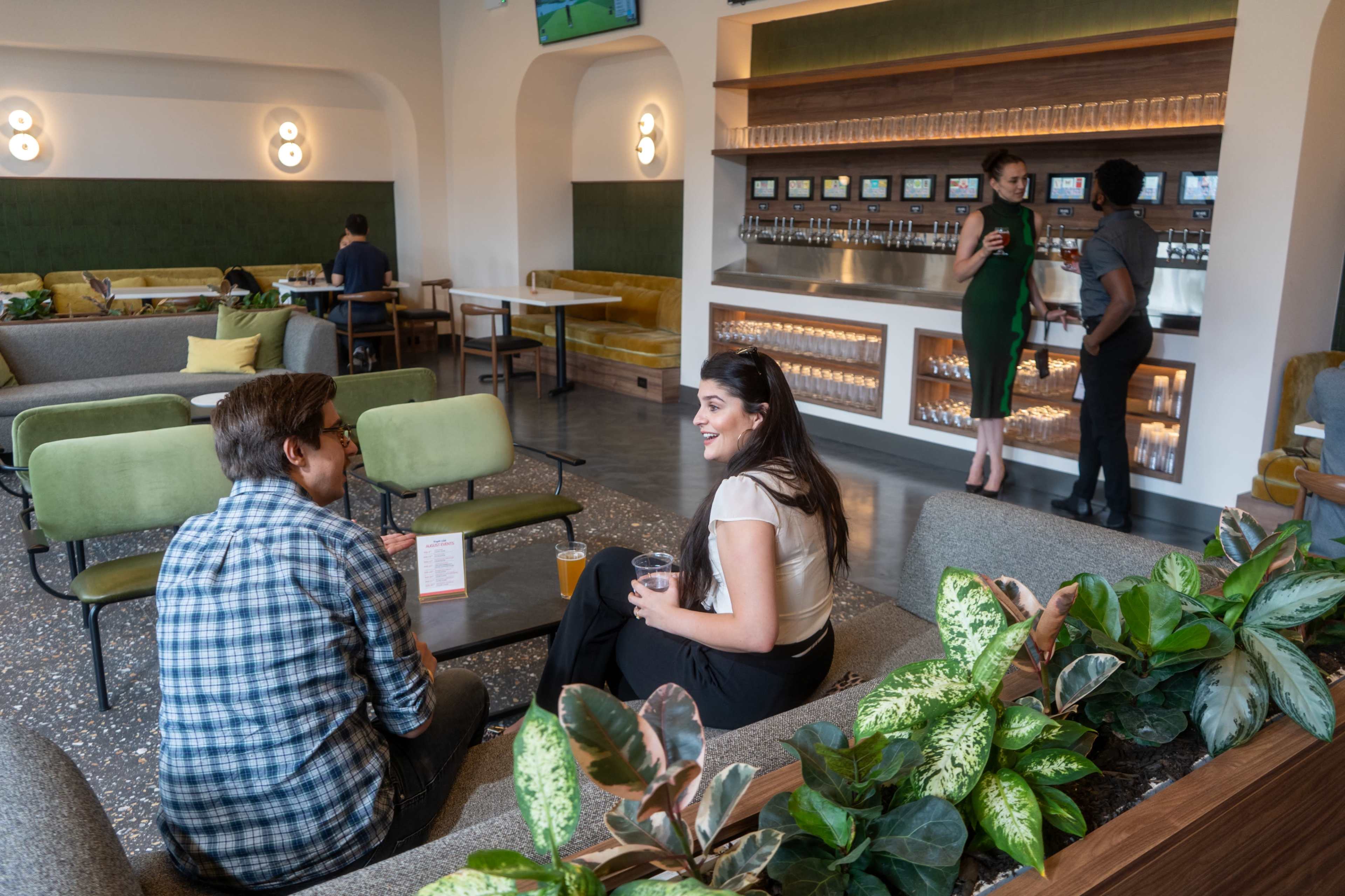 A couple sits at a cozy café, engaged in conversation while a server interacts with two customers at the bar in the background.