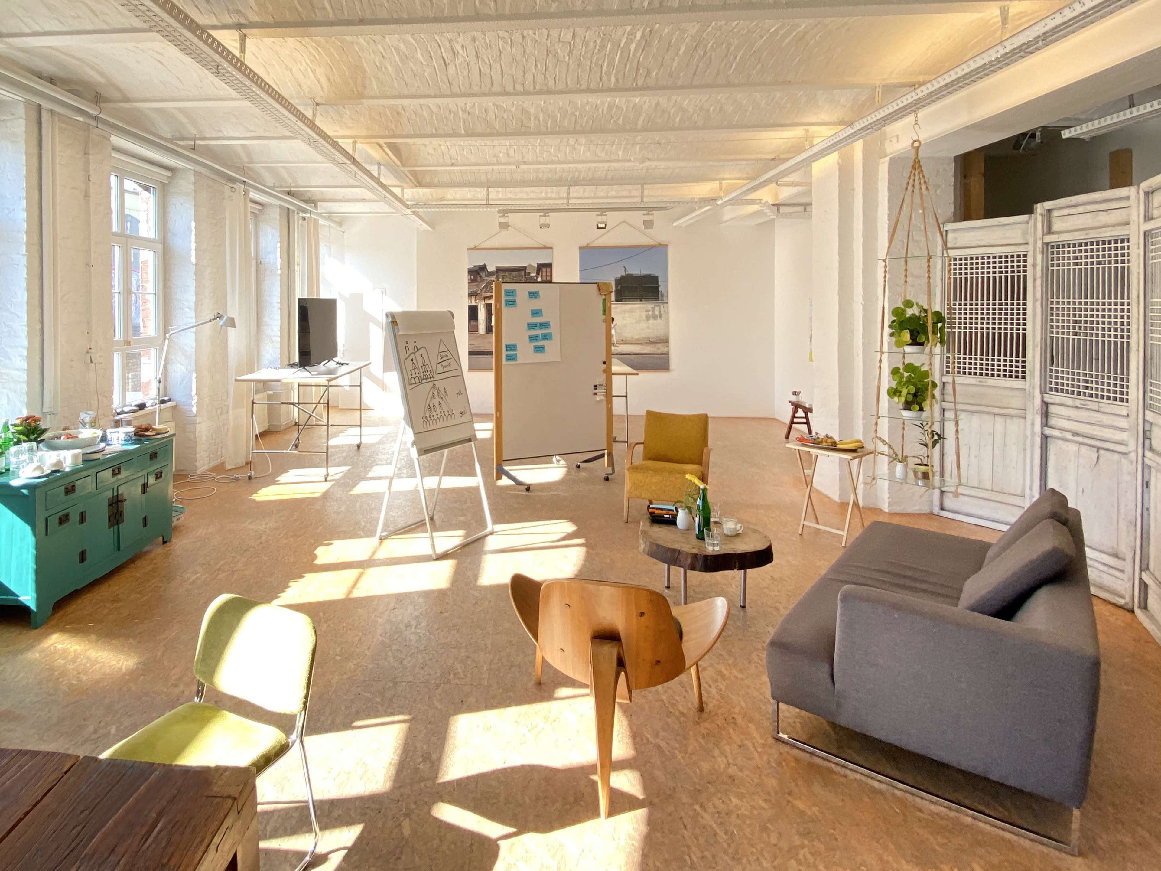 A spacious, well-lit office area featuring a mix of seating arrangements, a whiteboard, and decorative plants.