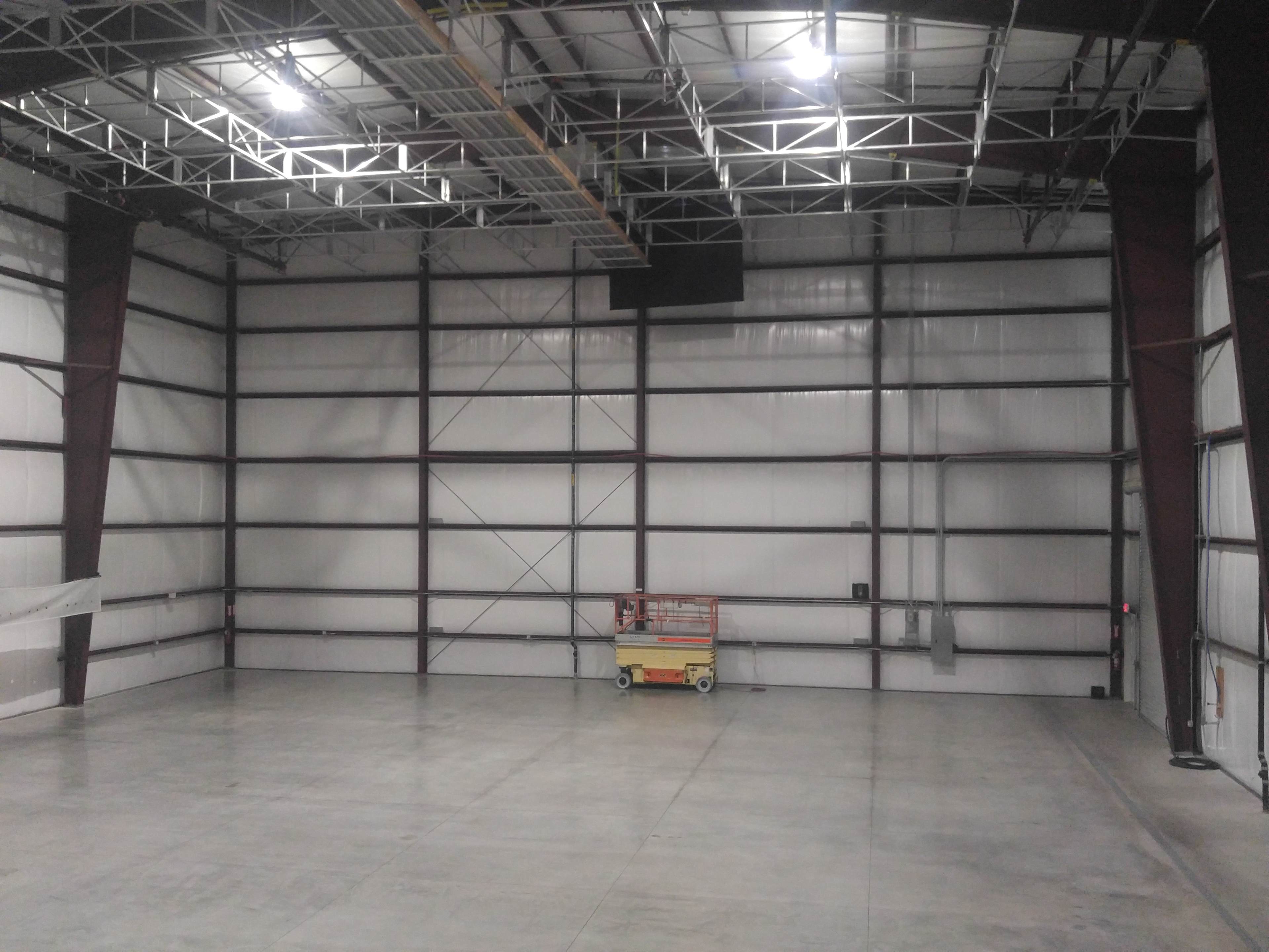 The image shows a large, empty industrial warehouse with concrete flooring and metal walls.