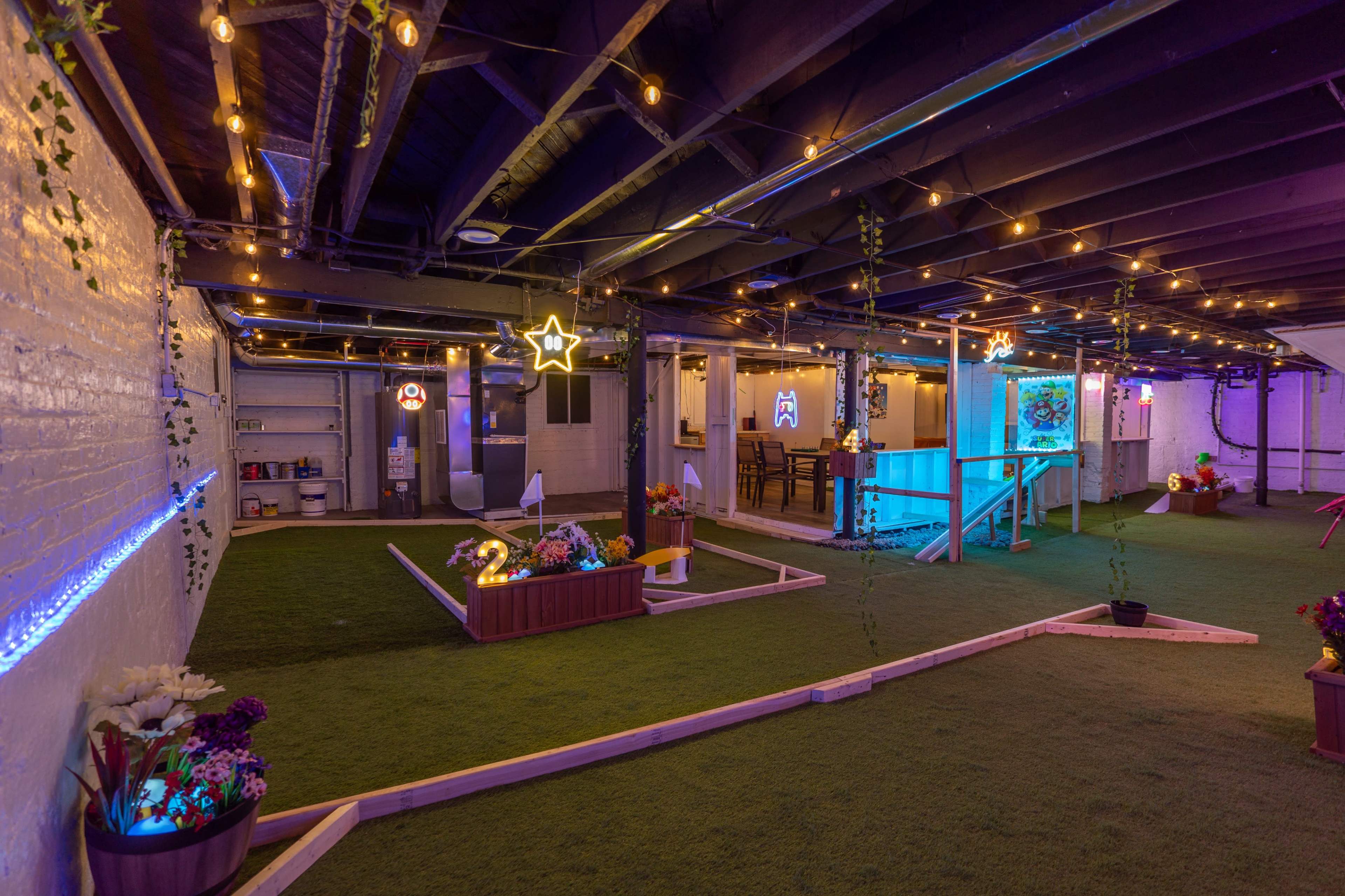 A spacious basement decorated with string lights and artificial grass, featuring flower planters, wooden structures, and a seating area.